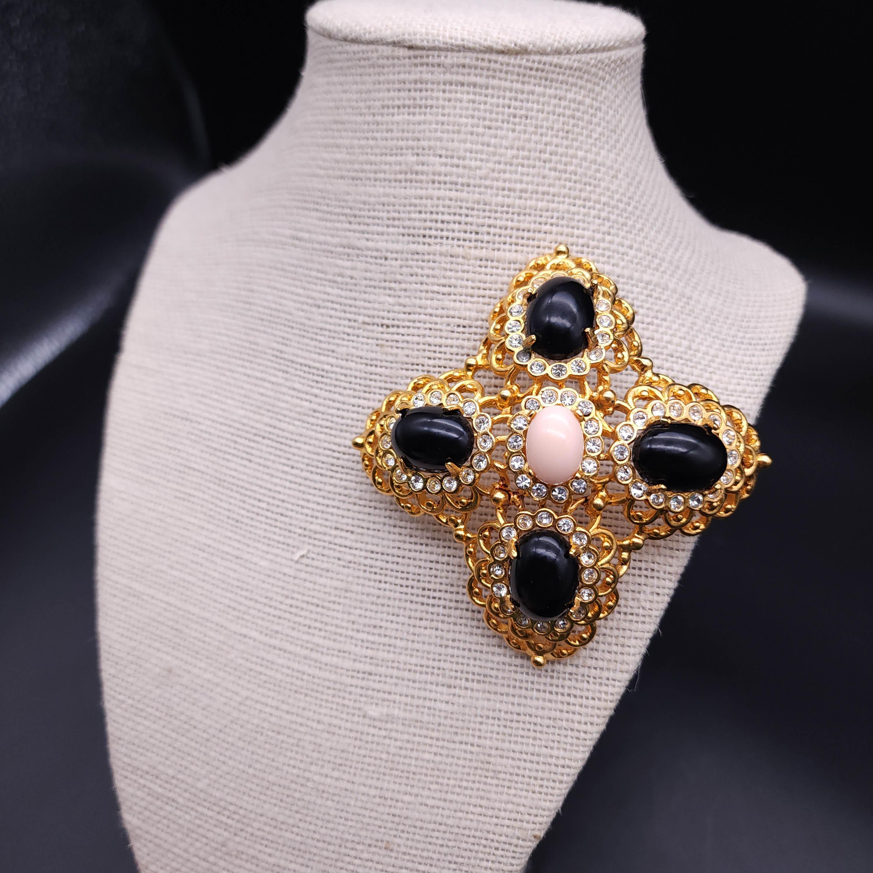 Elevate your ensemble with the Kenneth Jay Lane cabochon cross pin, a stunning accessory that exudes elegance and sophistication. This exquisite piece features a light pink centerpiece cabochon, gracefully encircled by four lustrous black cabochons.
