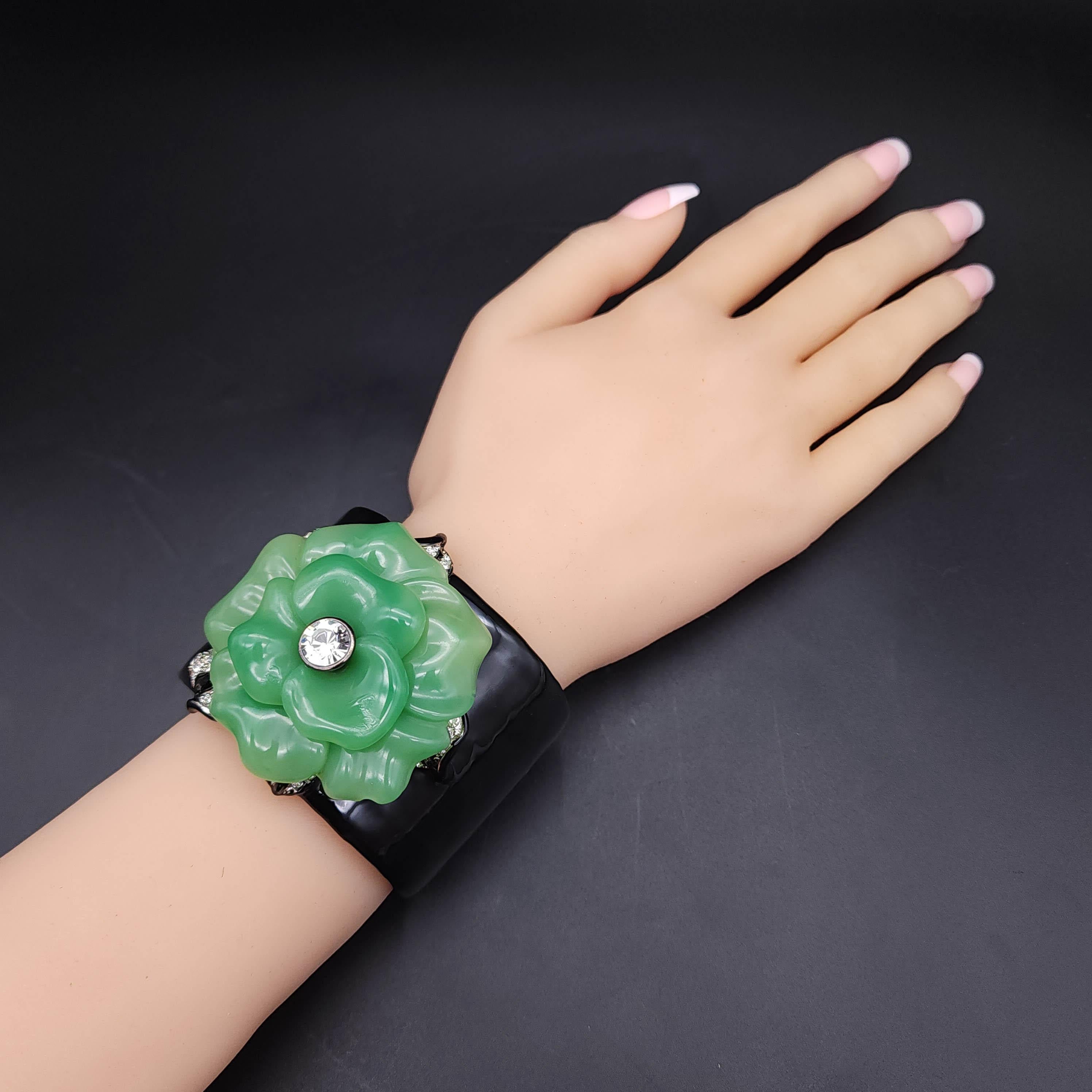Entrez dans le monde du luxe avec le bracelet manchette à fleurs en faux jade de Kenneth Jay Lane. Cette magnifique pièce présente un anneau audacieux de 2 pouces de large, orné d'une fleur de faux jade complexe et de cristaux clairs étincelants.