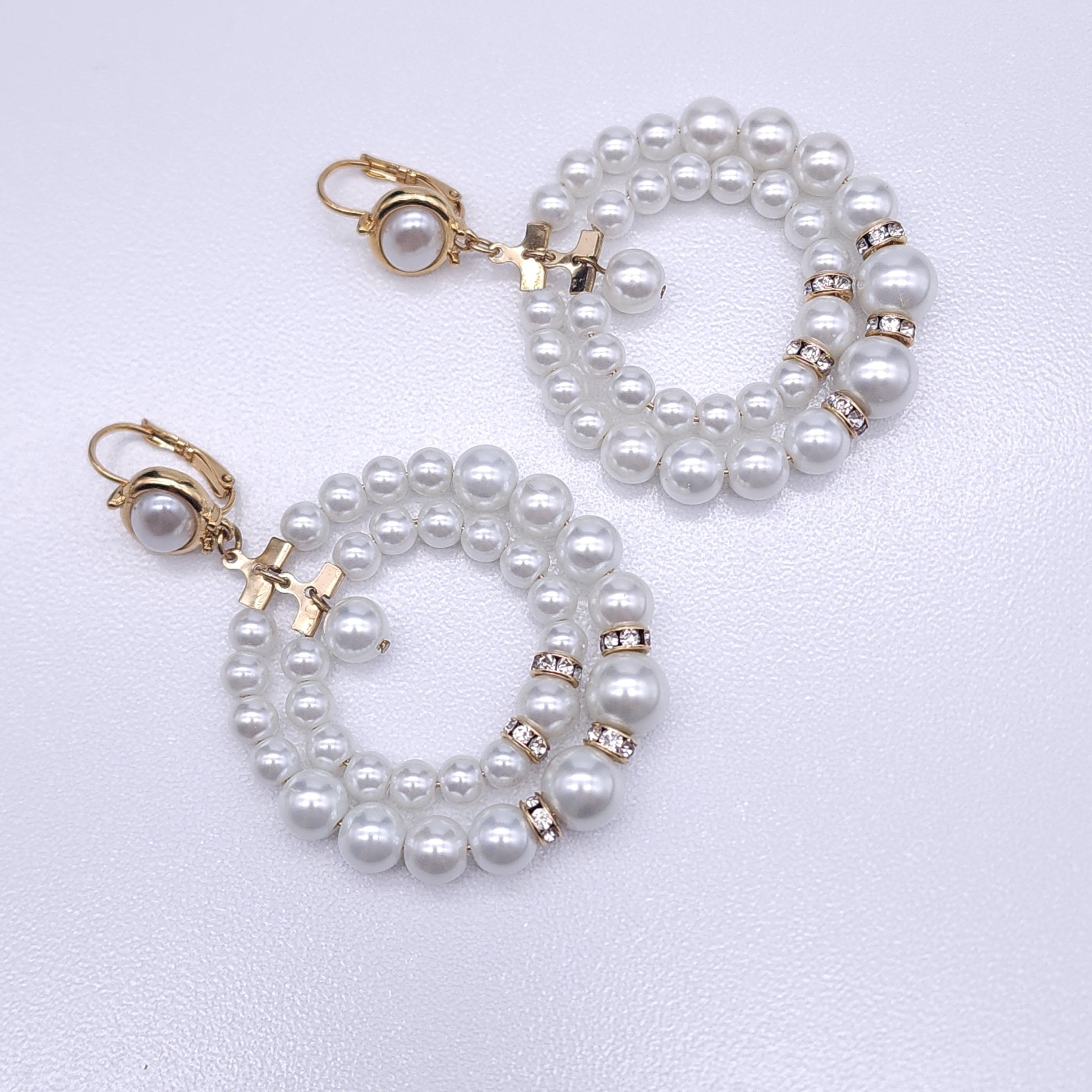 These elegant Kenneth Jay Lane double hoop earrings feature faux pearls with rhinestone accents on a gold-plated frame. The timeless design includes an oval faux pearl stud and clip-back fastening for secure wear. Perfect for adding a touch of
