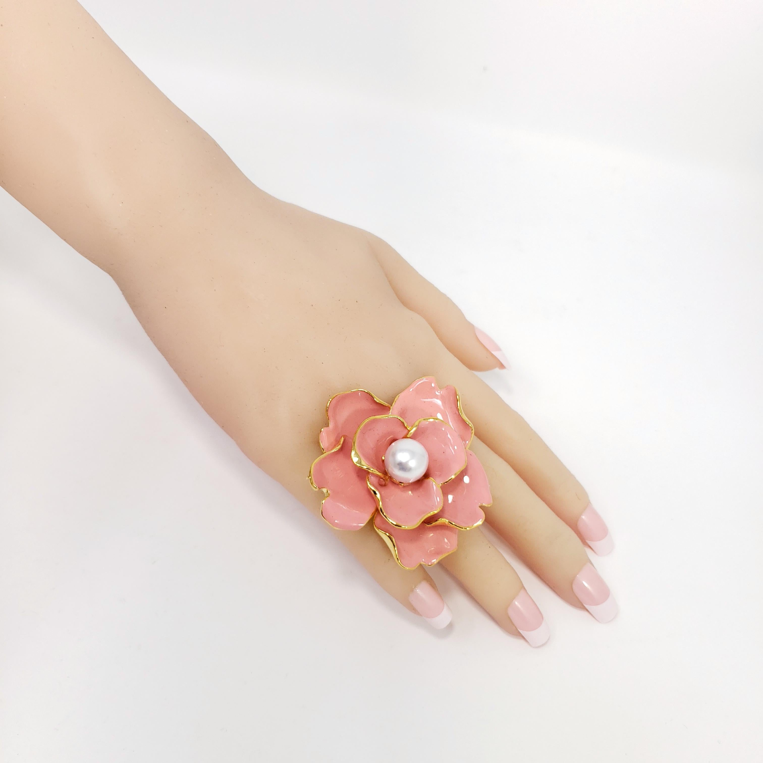 Floral elegance by Kenneth Jay Lane! A cocktail ring featuring a flower, painted in salmon coral enamel and accented with a single faux pearl.

Adjustable sizes 4.5 to 8 US

Gold plated. Made in USA.

Hallmarks: Kenneth Lane