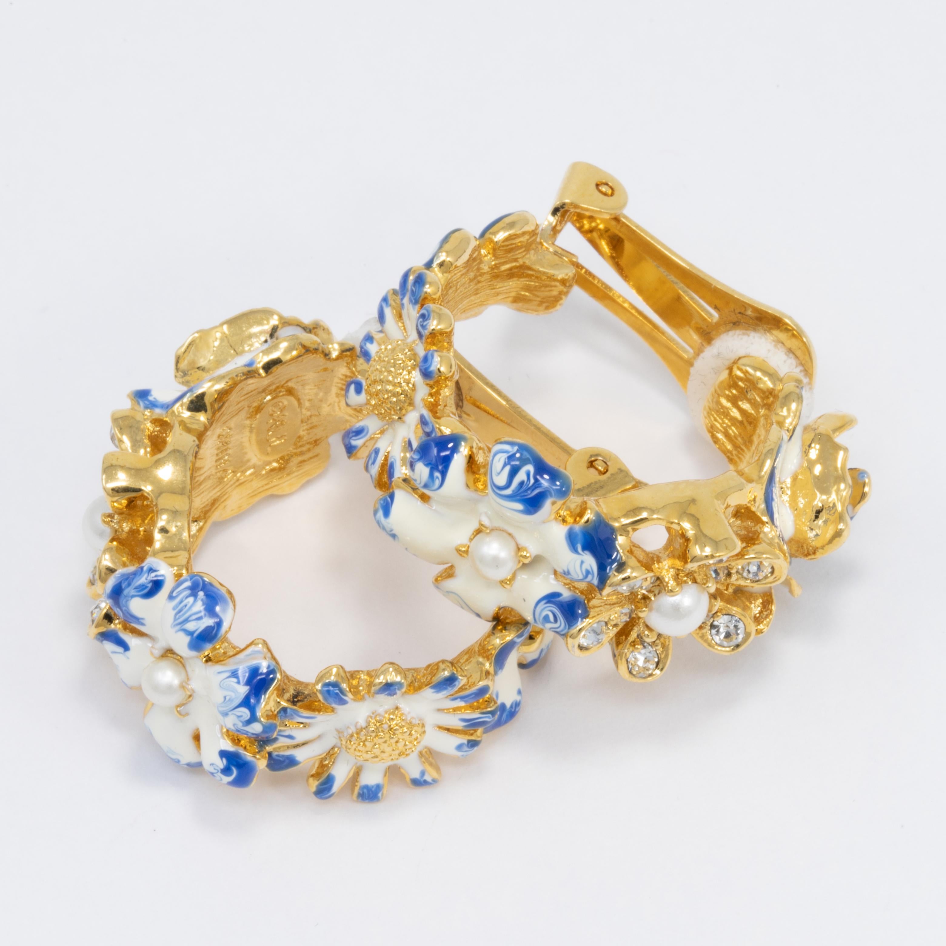 A pair of golden flower earrings, painted in white and blue enamel and accented with faux pearls & crystals. By Kenneth Jay Lane.

Hallmarks: KJL

Gold plated.