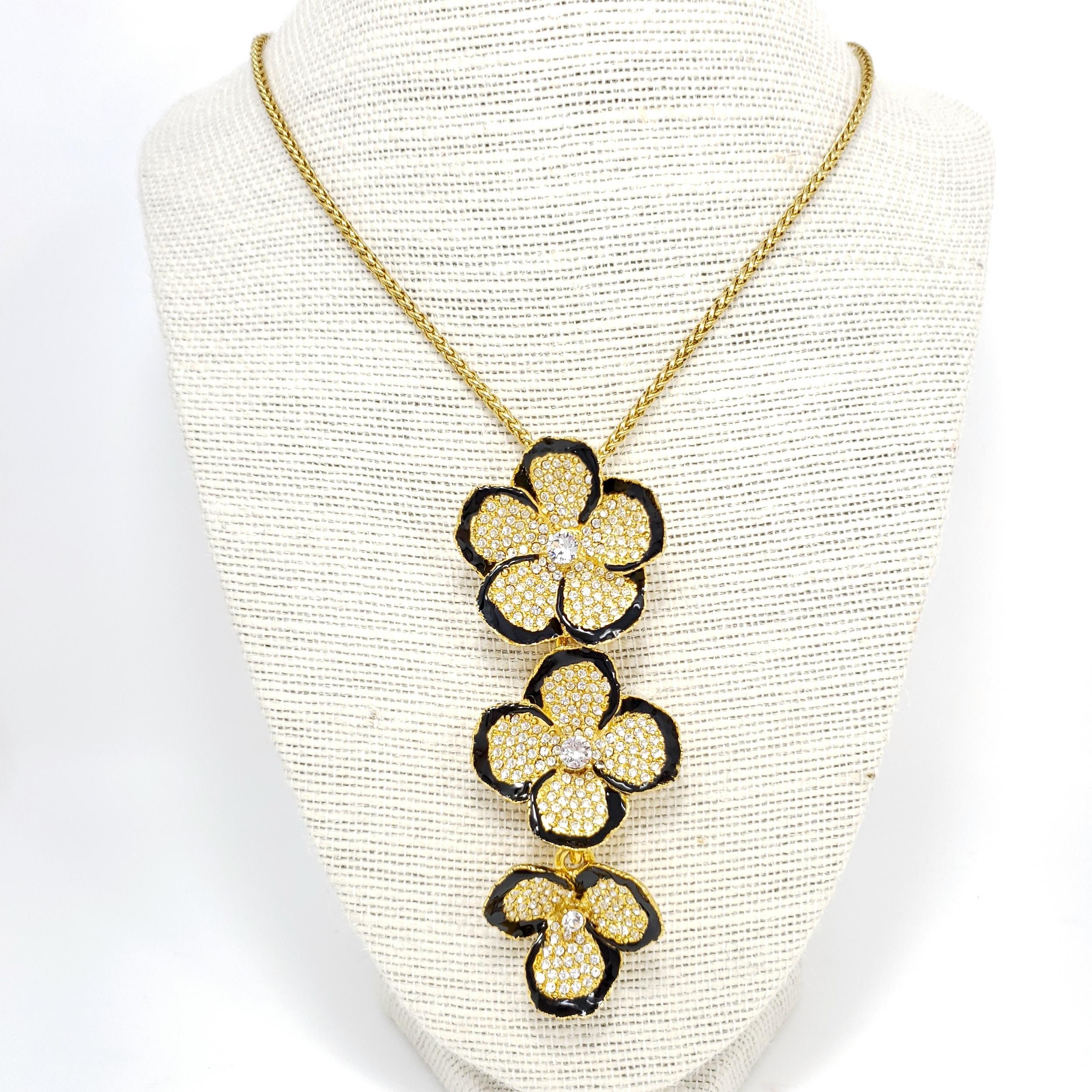 A three-link flower pendant hangs off a fine golden chain. Each flower is decorated with clear pave crystals and painted with black enamel for a striking contrast.

Gold plated.

Tags, Marks, Hallmarks: Kenneth Lane, Made in USA

Length: 26 inches