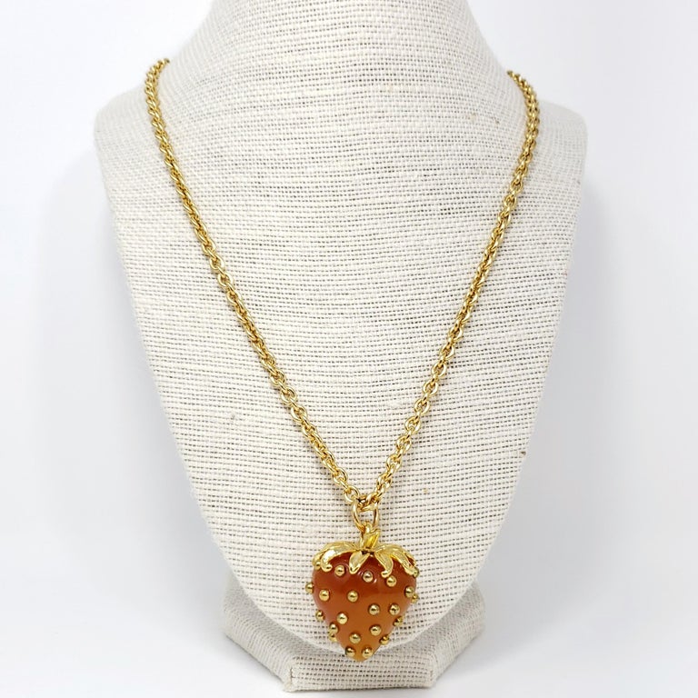 Amber colored strawberry accented with golden studs hangs on a long gold chain. Pendant necklace by Kenneth Jay Lane.

Gold plated.

Tags, Marks, Hallmarks: Kenneth © Lane

Length: 21 to 24.5 inches