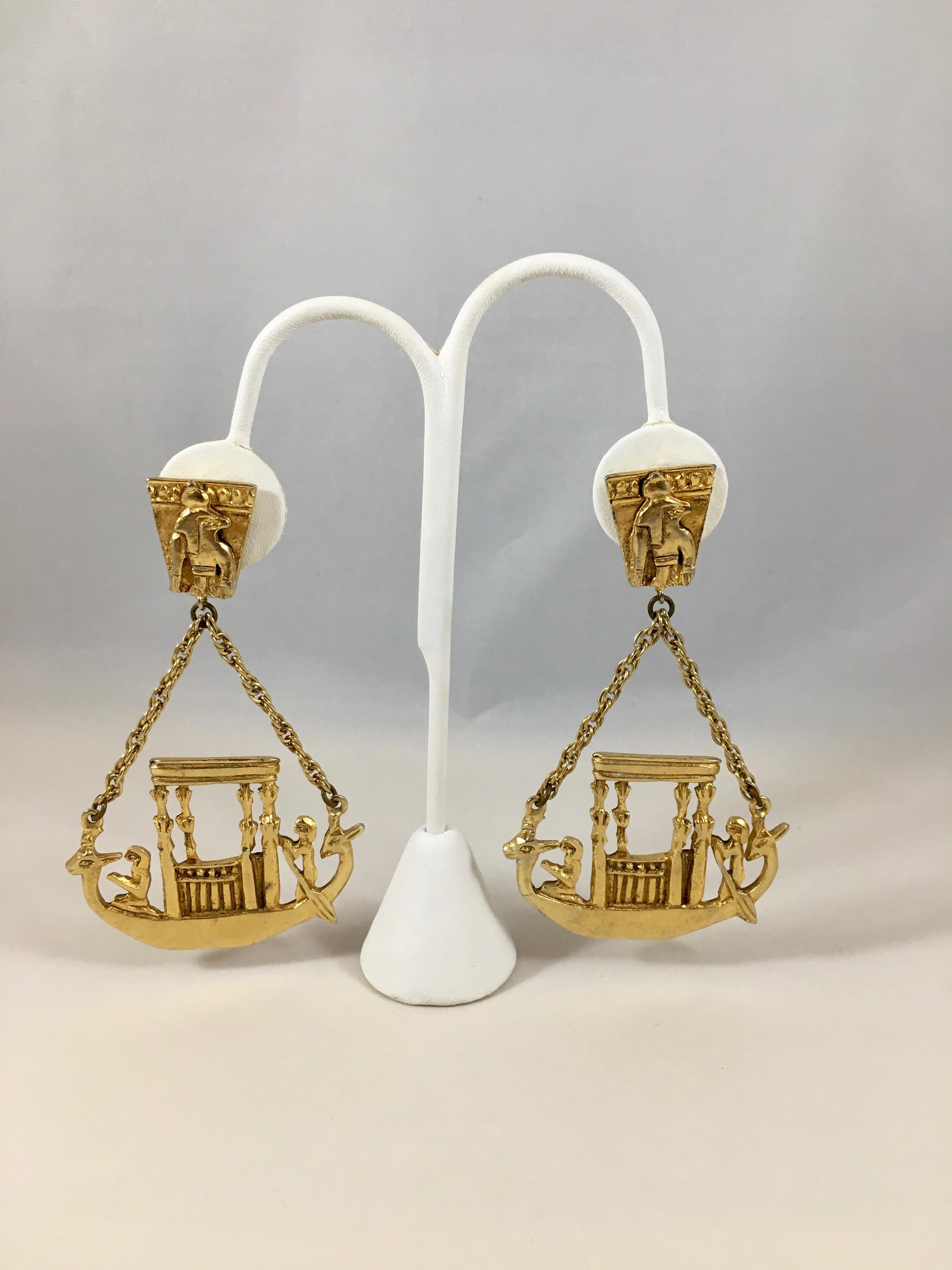 This is a show stopping pair of 1970s Kenneth Jay Lane Egyptian themed dangle earrings. They are gold-toned and each feature an ancient Egyptian ship with Egyptian gods on board. The earrings measure 3 1/2 inches long x 2 inches wide. They are in