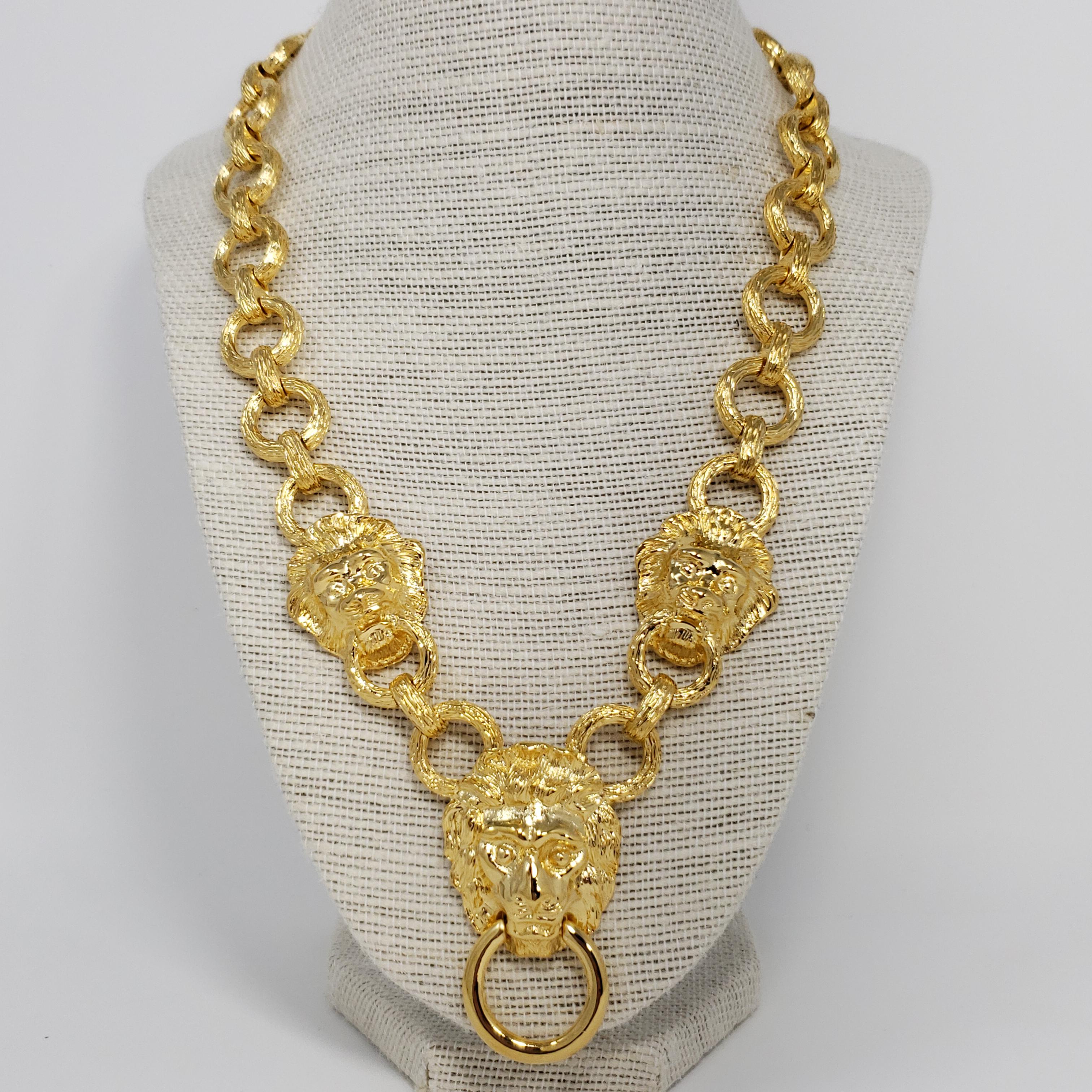 Bold stylish lion pendant necklace by Kenneth Jay Lane. Features textured golden links decorated with lions' heads on each side. The pendant lion's head holds a door-knocker style ring.

Hallmarks: KJL