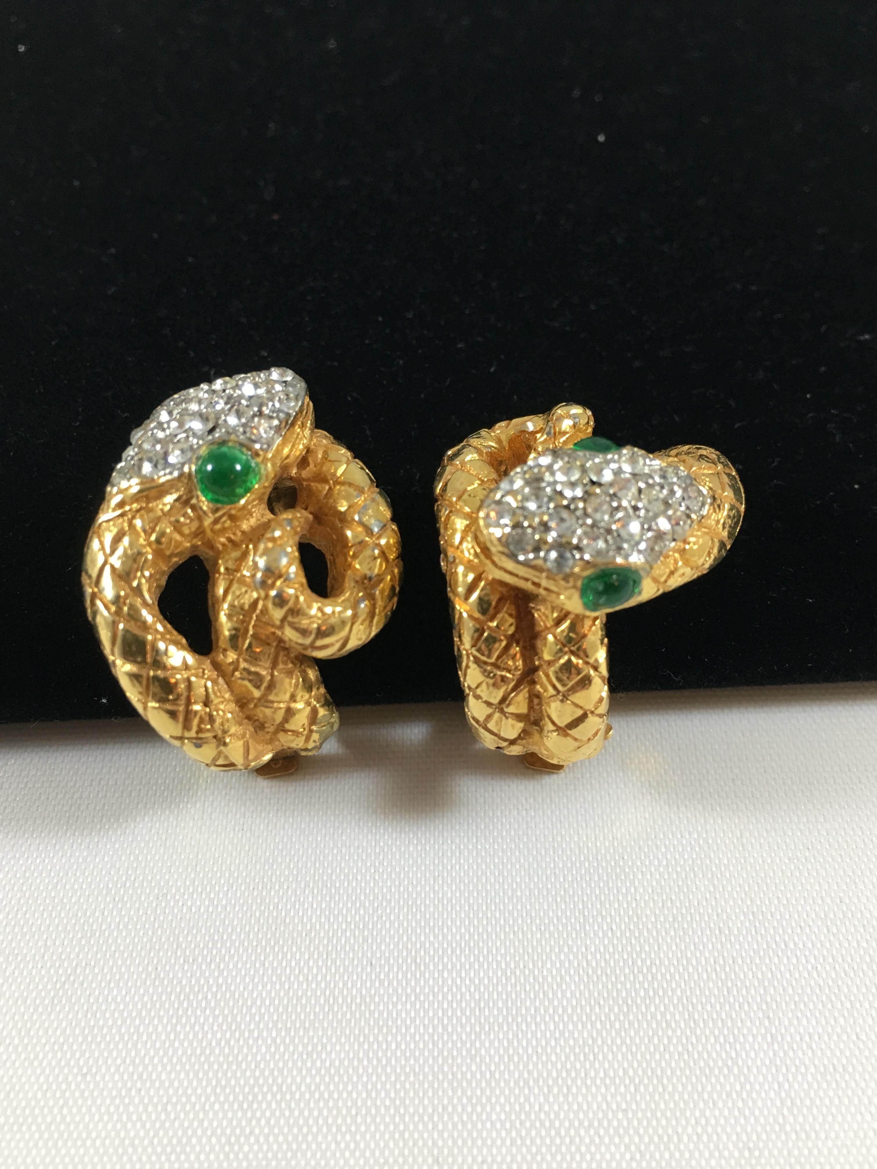 This is a gorgeous pair of 1960s Kenneth Jay Lane snake clip-on earrings. Each earring is different from the other. They are made so that both of the snakes' faces face inward towards the wearer. The snakes are gold-toned and set with clear pave
