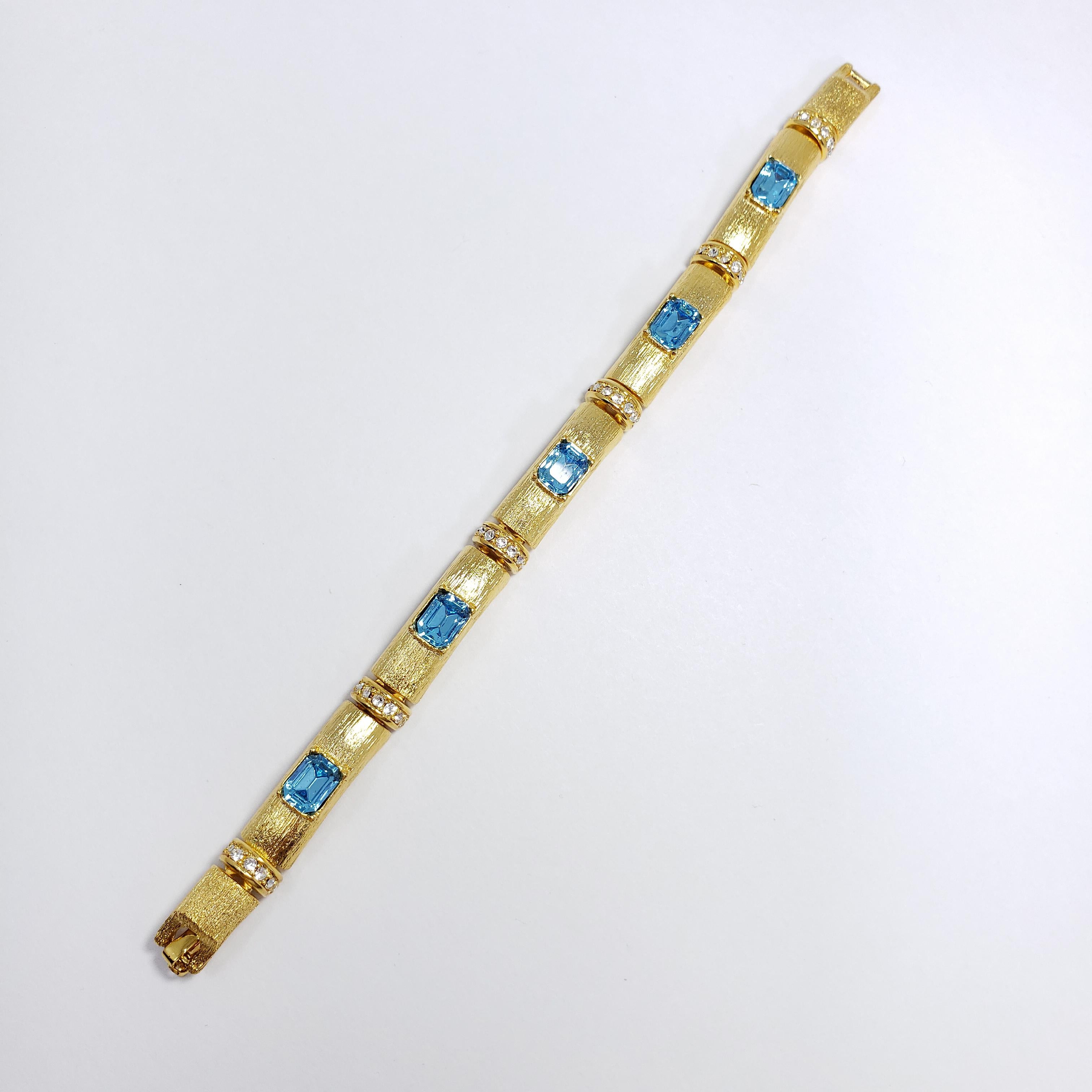 Ein stilvolles Armband von Kenneth Jay Lane in Goldton, das aus miteinander verbundenen, strukturierten Segmenten besteht, die mit klaren und blauen Kristallen verziert sind.

Markenzeichen: Kenneth Jay Lane