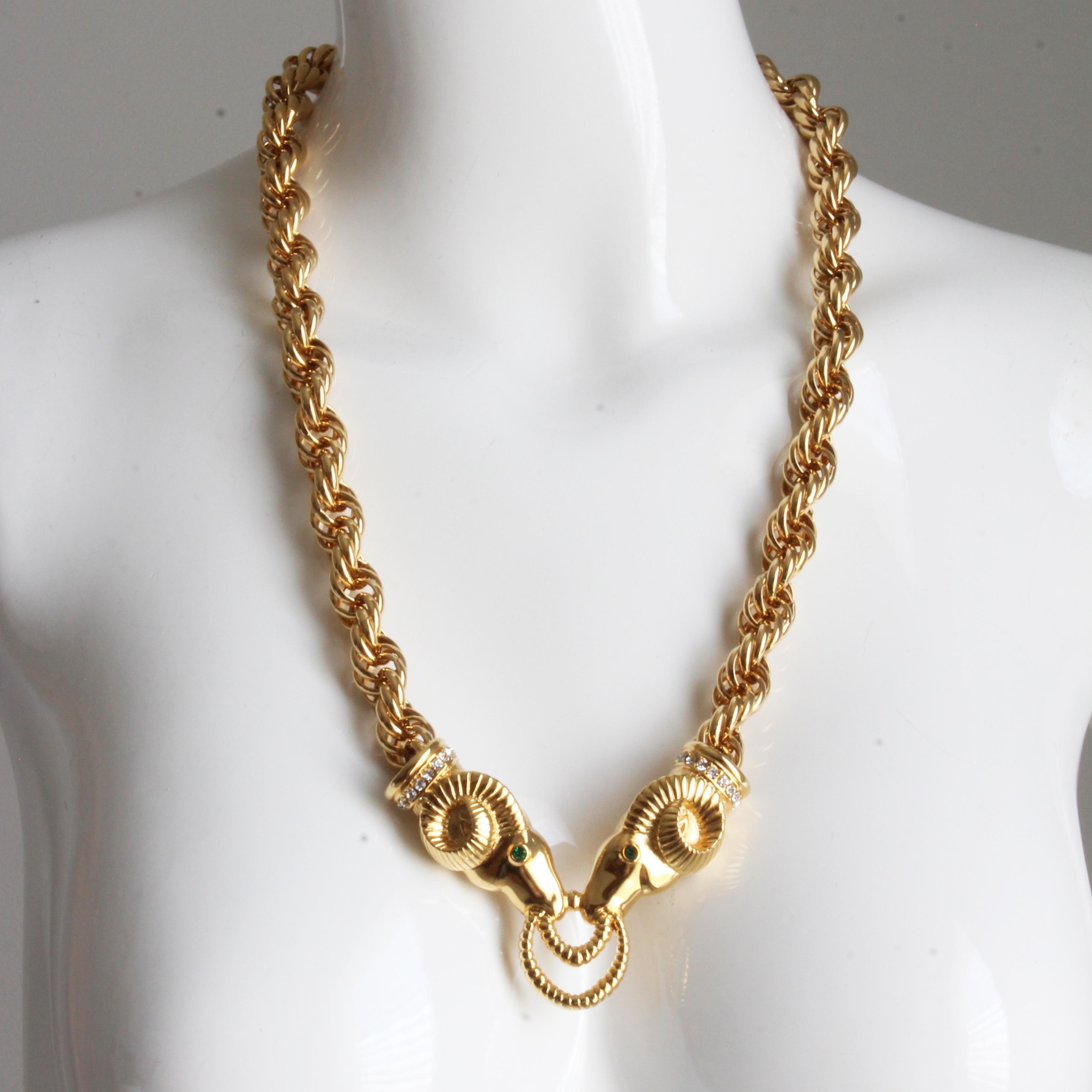 Preowned, vintage Kenneth Jay Lane necklace with embellished ram heads, likely made in the 90s. Made from gold metal, it features a chunky triple link chain with extender, and two gold metal ram heads with green rhinestone eyes and white rhinestone