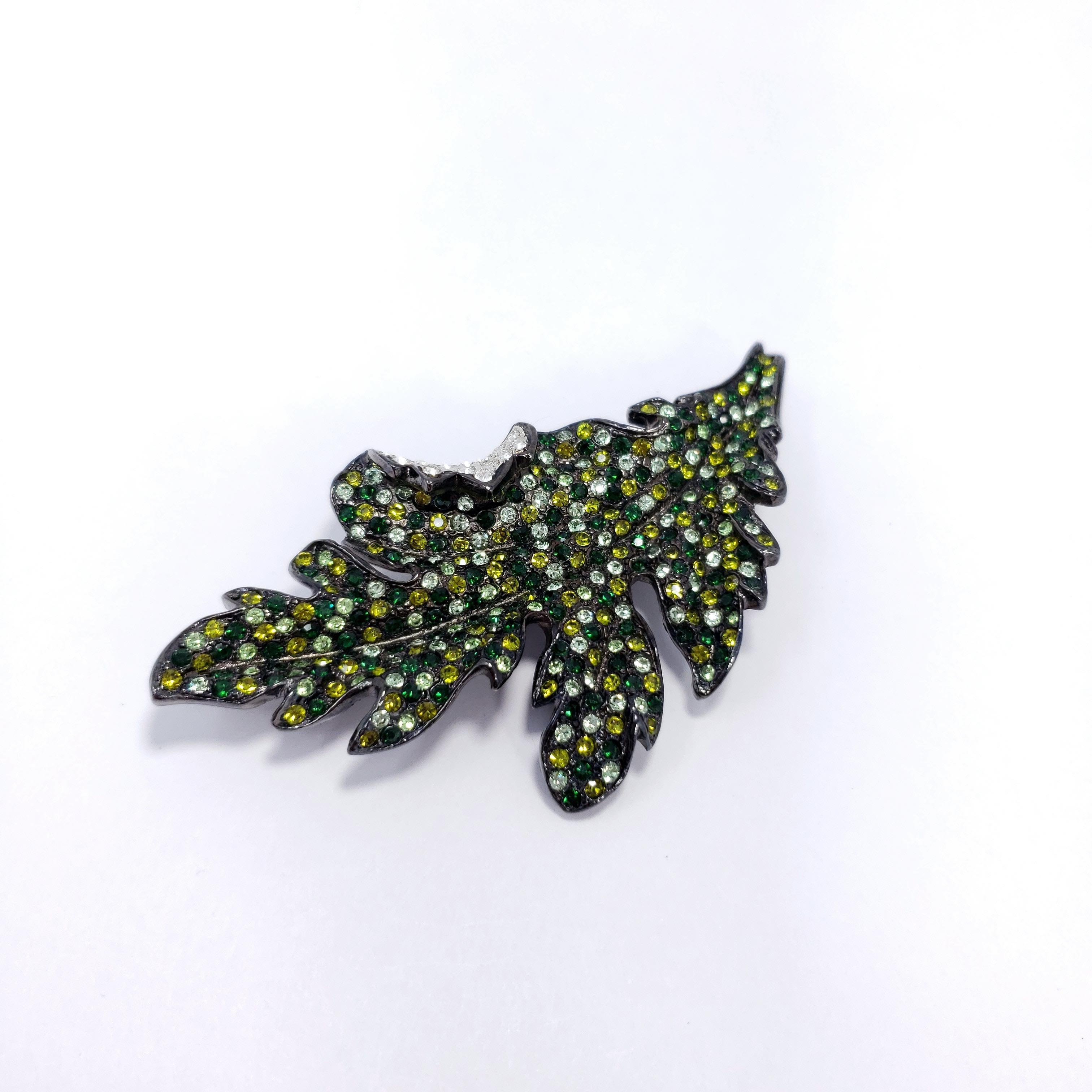 Sparkling pin brooch from Kenneth Jay Lane. This gray-gunmetal leaf is decorated with dazzling crystals in peridot, olivine, and emerald colors.

Hallmarks: Kenneth Lane