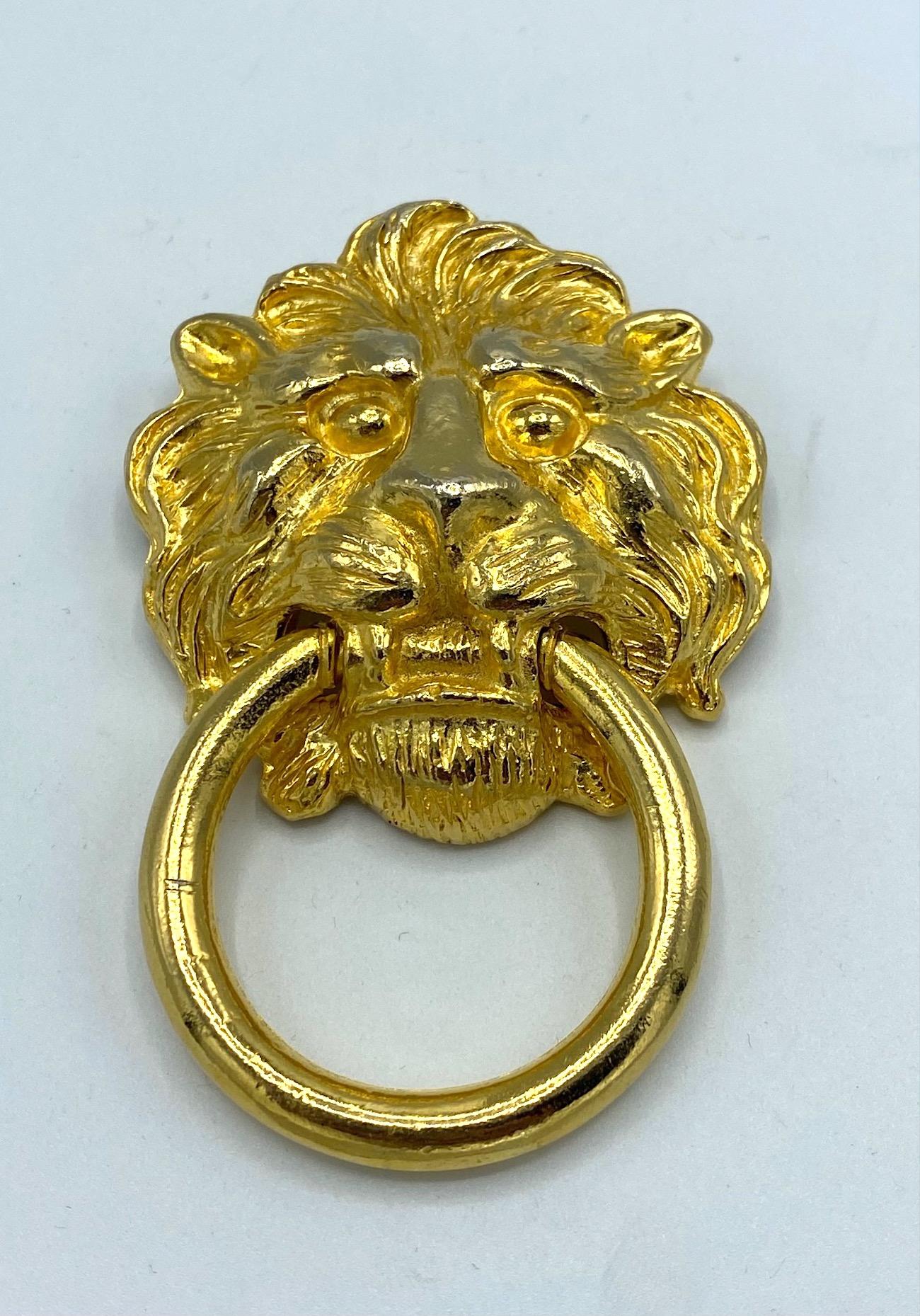 A very very nice and classic lion face with ring door knocker style brooch from the 1980s by Kenneth Jay Lane. It is beautifully cast and carved with attention to the lion's mane and plated in a rich warm gold. The 1.75 inch diameter ring hangs