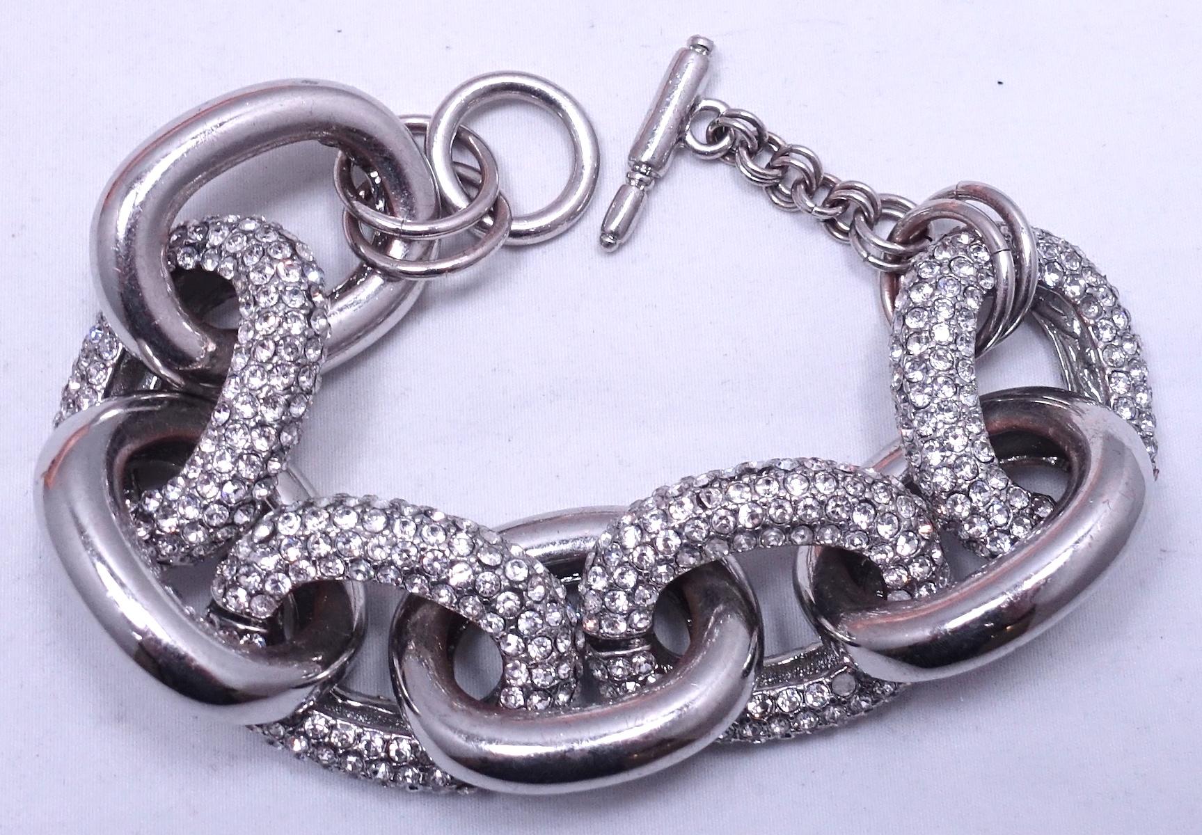 This Kenneth Lane bracelet features a link design with clear crystal accents in a silver tone setting.  In excellent condition, this bracelet measures 9” x 1-1/8” with a toggle bolt closure. 