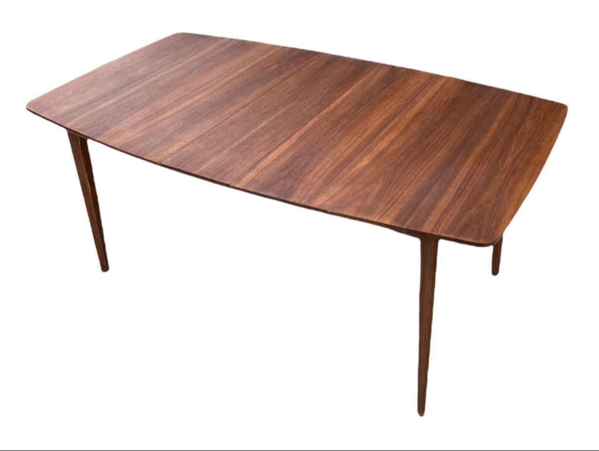 Beautiful and versatile dining table, executed in American black walnut by American modern manufacturer Kent-Coffey. Versatile design with included leaf. All segments with same color and finish. Original lawyer has been stripped. Surface has been