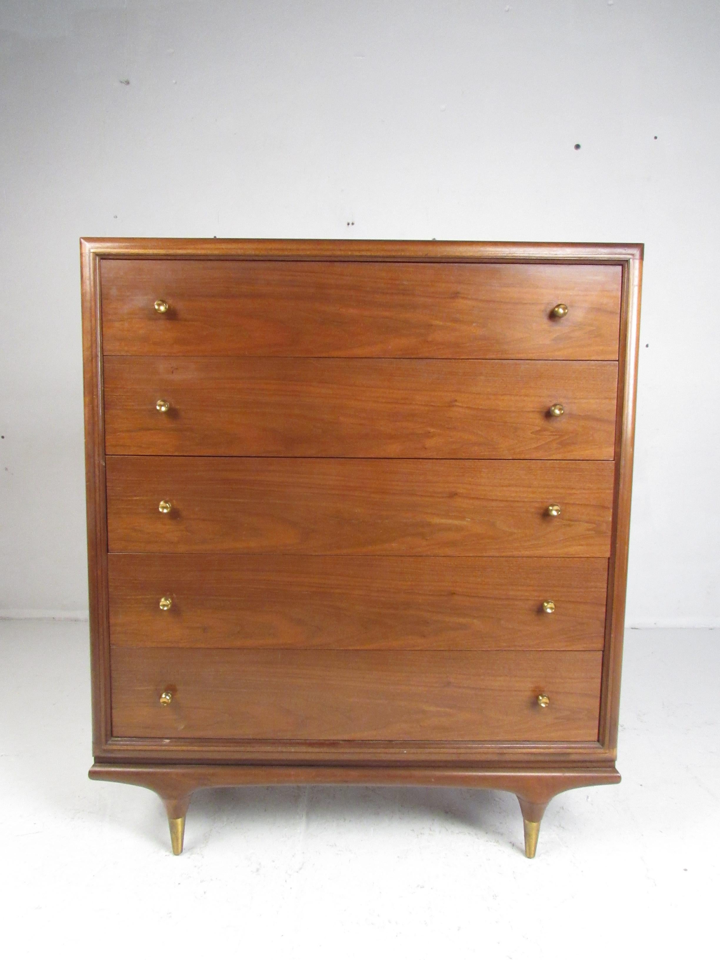 This stunning Mid-Century Modern dresser by Kent Coffey features five hefty drawers ensuring plenty of room for storage. A well constructed piece that sits on four stubby tapered legs with brass capped feet. The straight lines, elegant walnut wood