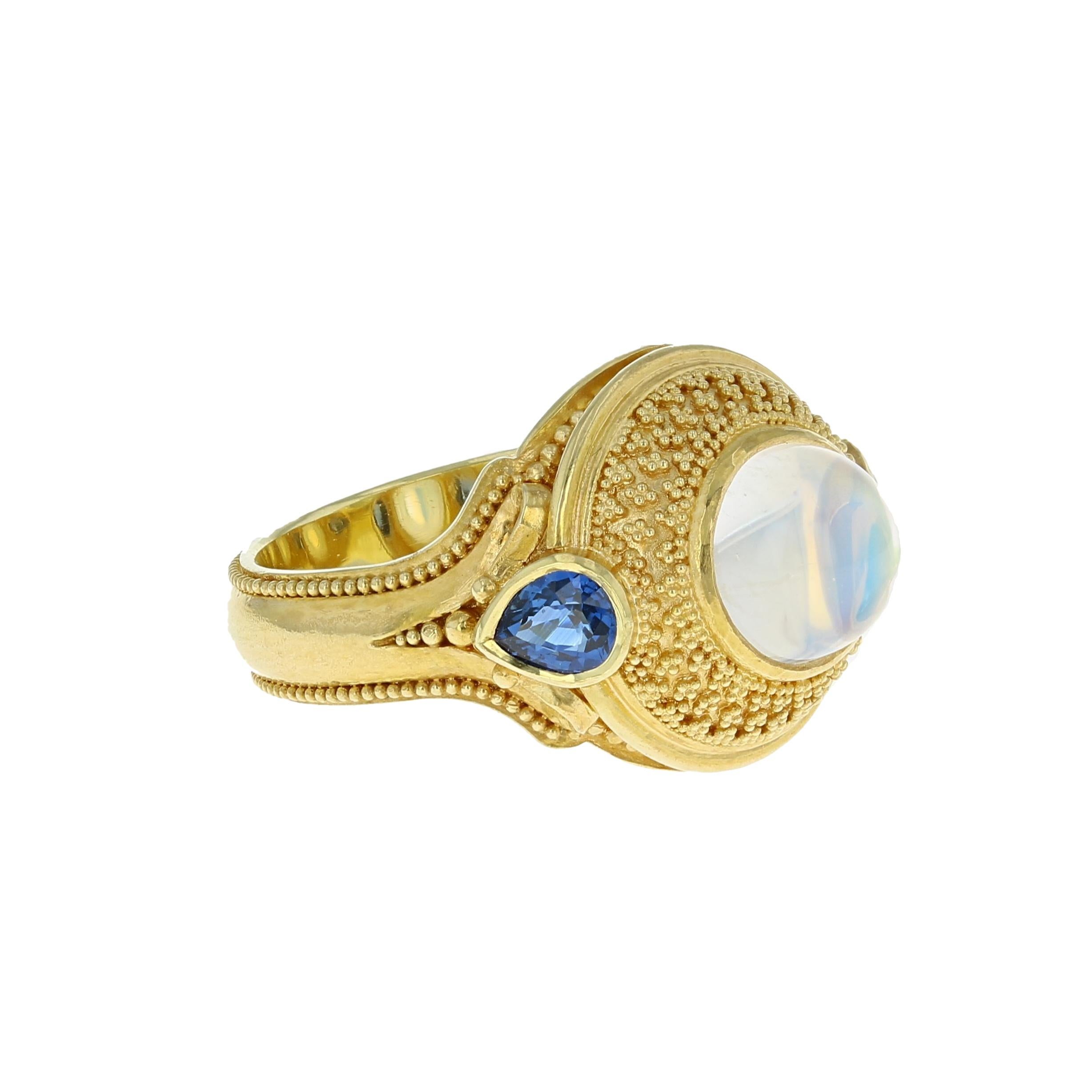 Kent Raible is at it again! He has created a stunning work of wearable art in his newest bespoke ring. Designed and hand crafted by the artist himself, this Rainbow Moonstone and Blue Sapphire ring has all the unique, intricate design and fine