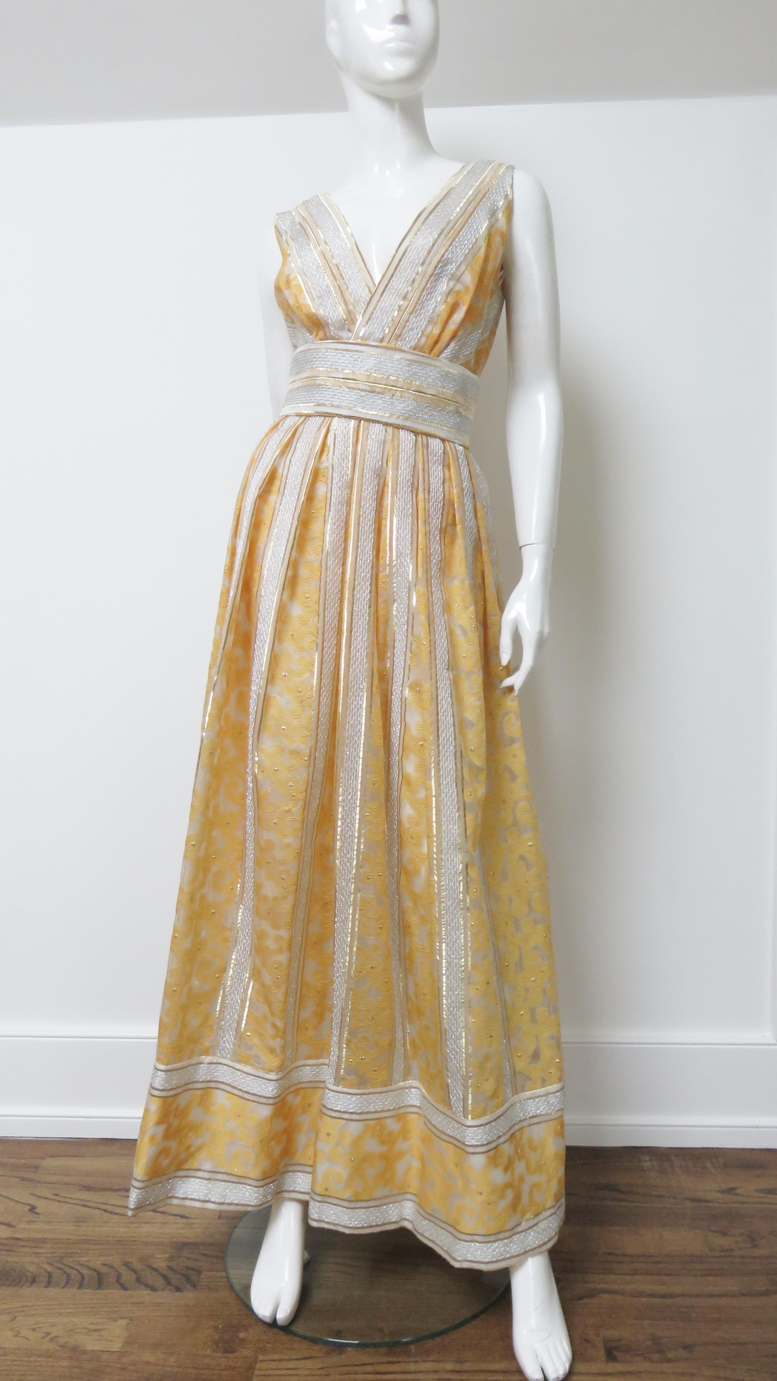 A beautiful silk gown from Kent Originals made in 1960s British Hong Kong.  The fabric consists of vertical panels of golden orange scrolls and geometric pattern against a sheer off white background with dots and lines of shot silver threads.  It