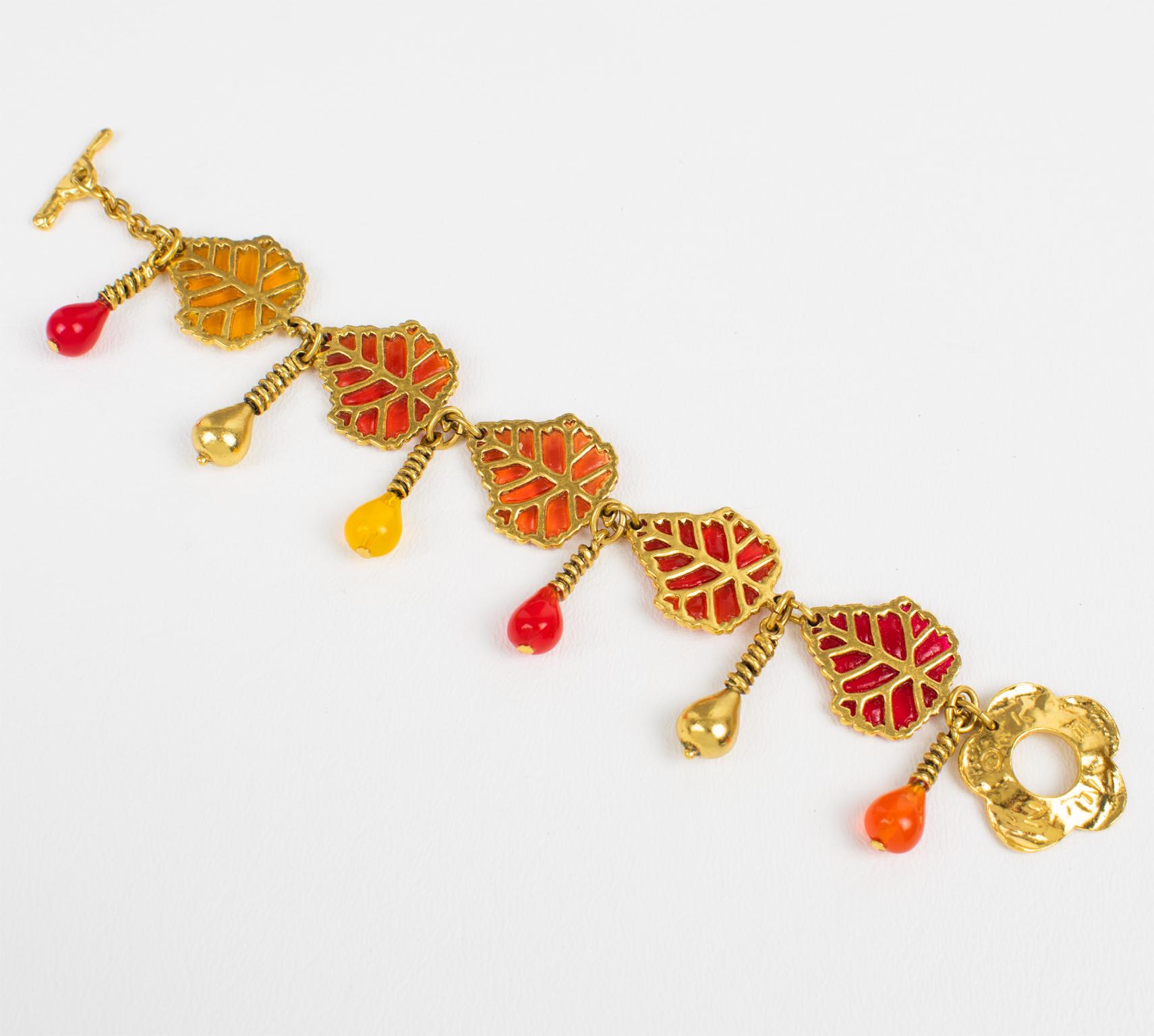This mesmerizing Kenzo Paris floral link bracelet features carved gilded metal framing with resin leaves and dangling charms. The bracelet closes with a floral toggle closing clasp. Each leaf has a different color and the bracelet has gradient
