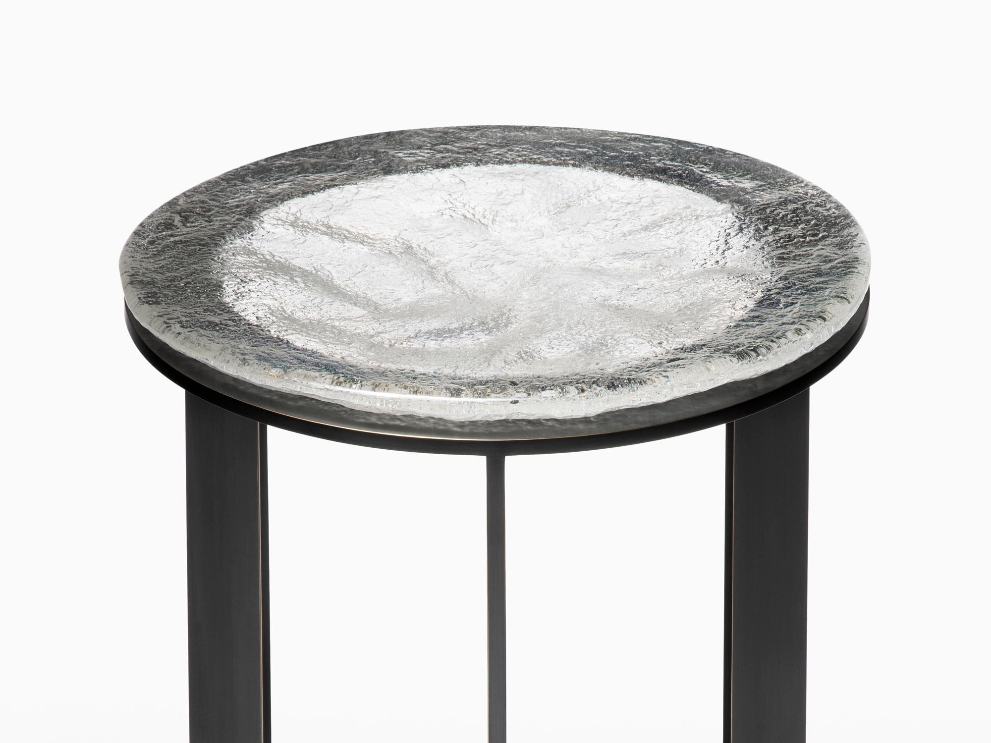 Artisan sand cast glass and expert metalwork highlight the Kepler Side Table. The cast glass top is produced using a ladle-poured casting process where molten glass is poured into a sand mold by expert glass artisans. The result is cast glass with a