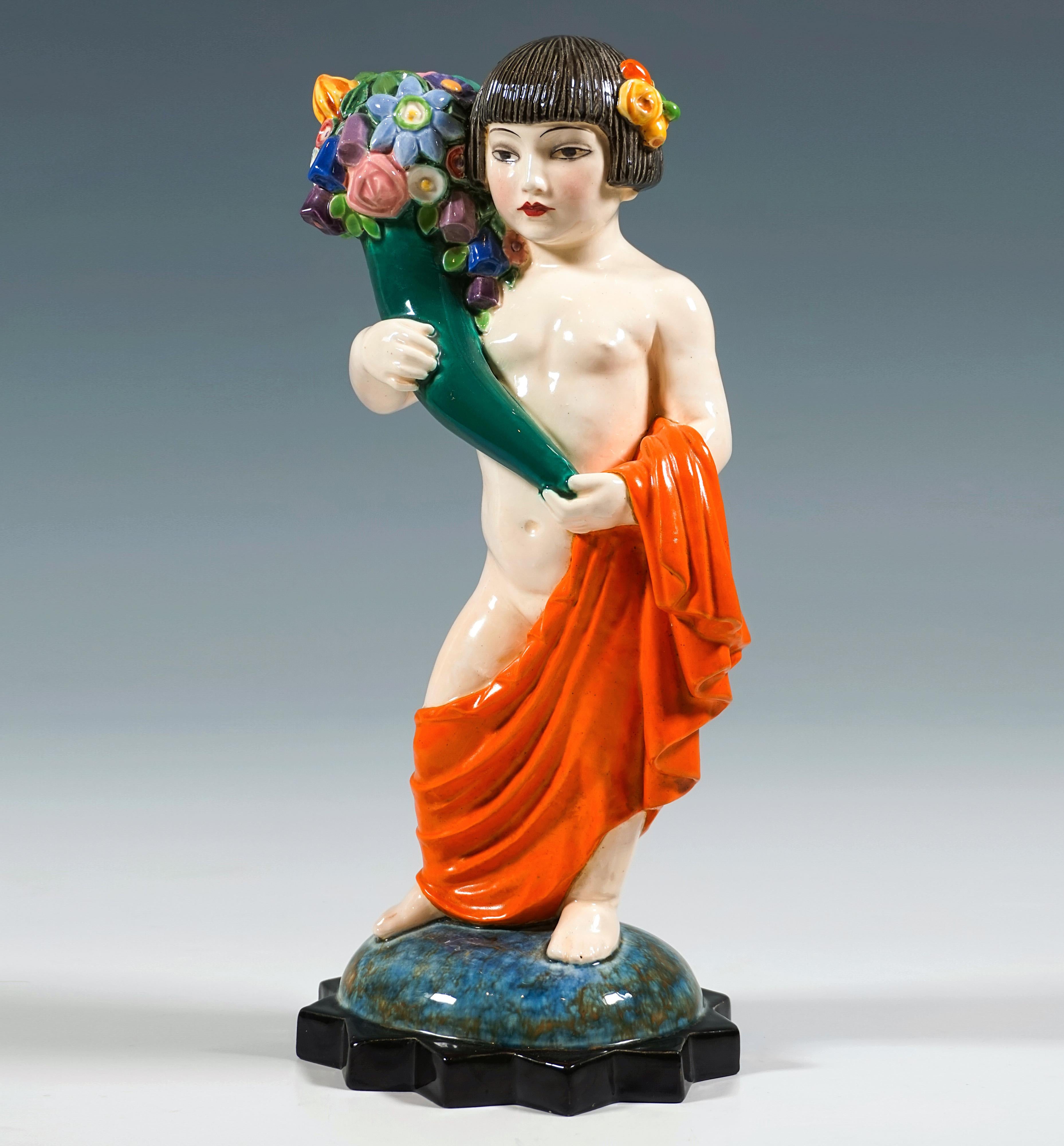 Rarísima figura vienesa de cerámica Art Déco:
Niña japonesa con un peinado de paje adornado con flores, de pie, llevando sólo una tela de color rojo anaranjado colgada alrededor de las caderas,  sosteniendo una cornucopia llena de flores de colores