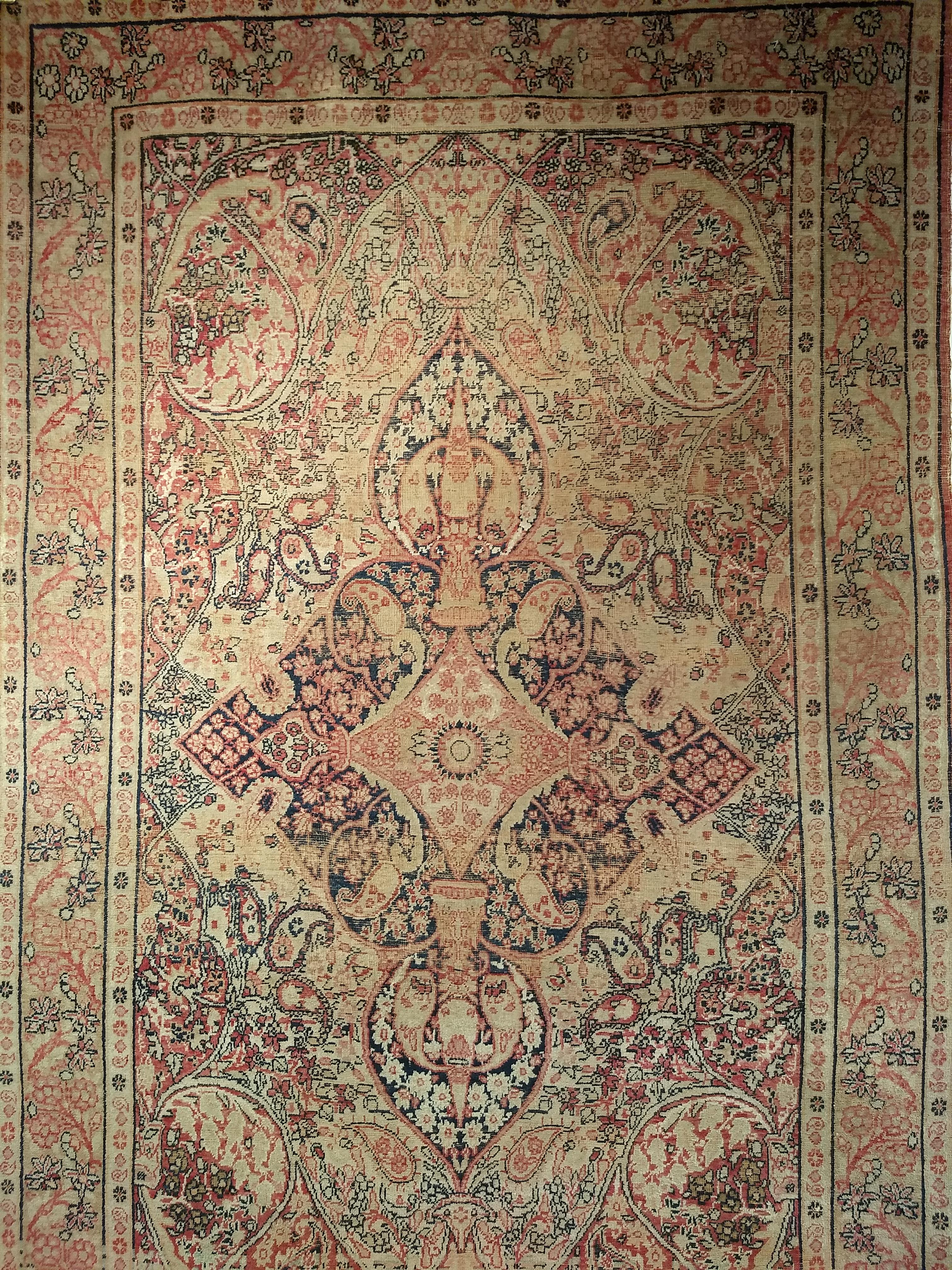 Beautiful vintage Persian Kerman Lavar area rug in a floral pattern from the late 1800s. The rug has a cream or pale yellow field and border color with curvilinear designs in red, black, and brown colors throughout. The village Lavar is near the