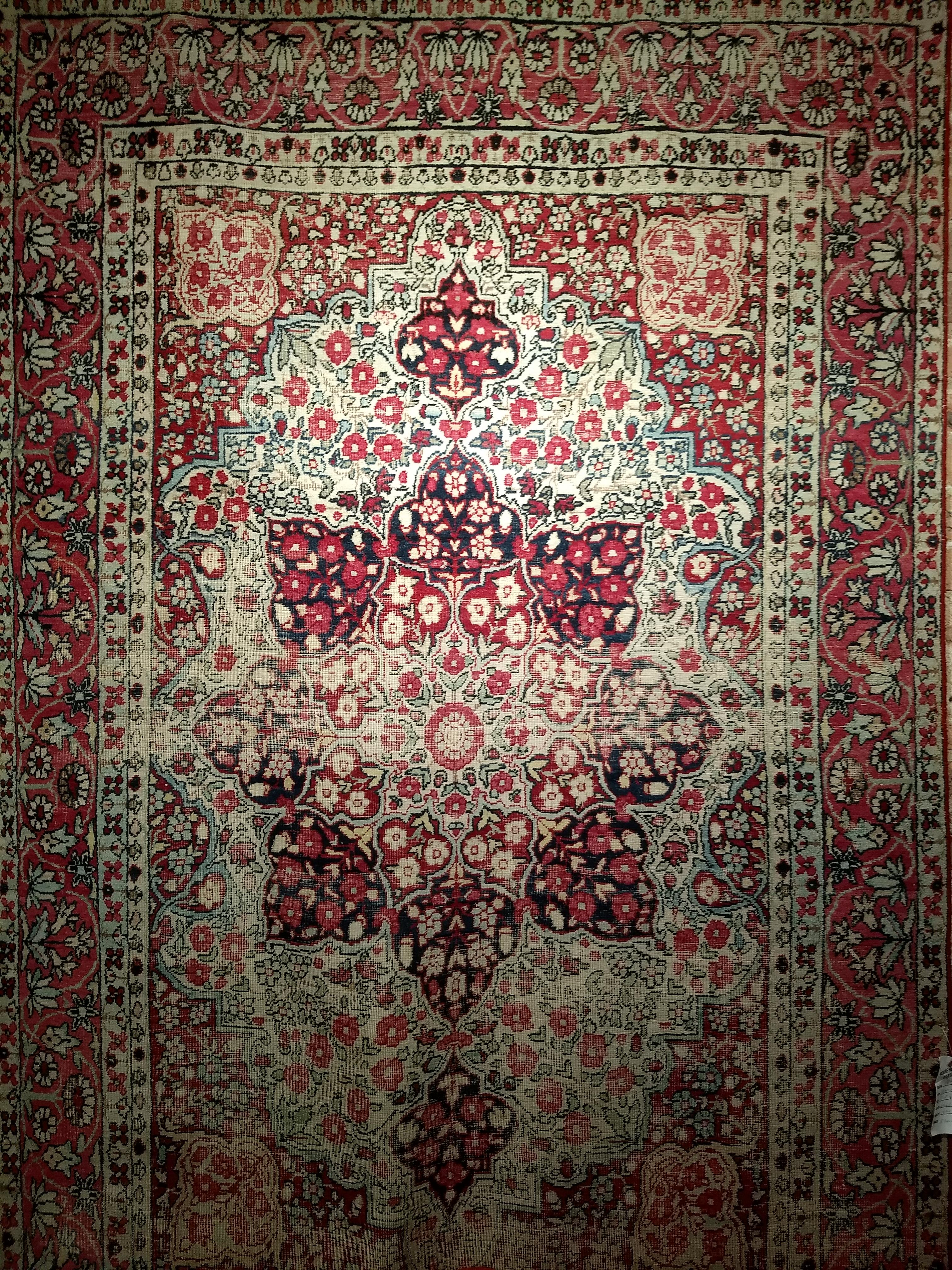 A beautiful Kerman Lavar rug from the late 1800s. The main field is in an ivory color with the corner spandrels in red and a rose red color border. The rug has a floral design in red, light blue, and cream colors. The border is in red color with