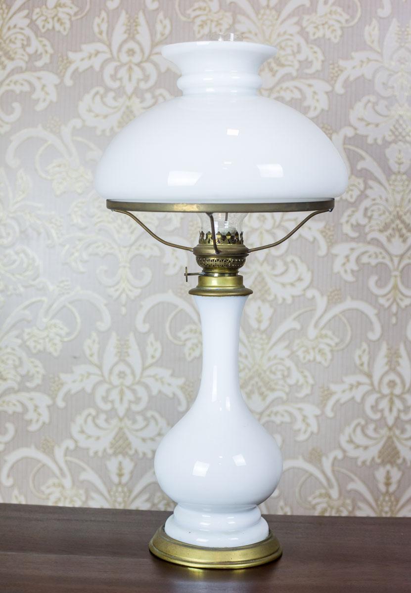 We present you this kerosene lamp from the 1930s, converted into an electric lamp.
Both the base and the shade are made of milk glass.
The shade holder, collar, and the knob are made of brass.

Presented item is in very good condition. The glass