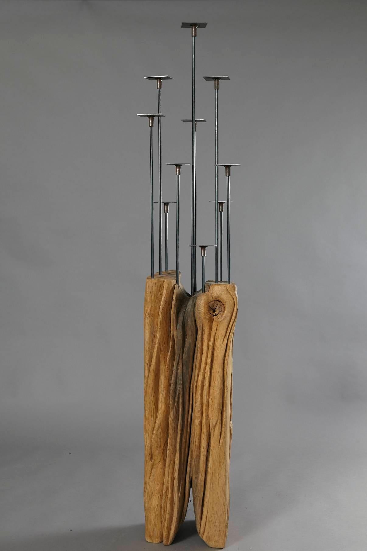 Kerzenständer - Candelabra 
Candelabra made from a solid piece of oak with welded black steel arms and plateaus for candles in different heights inserted into the oak, by German artist Hanni Dietrich. 
All wood used by the artist is from salvaged