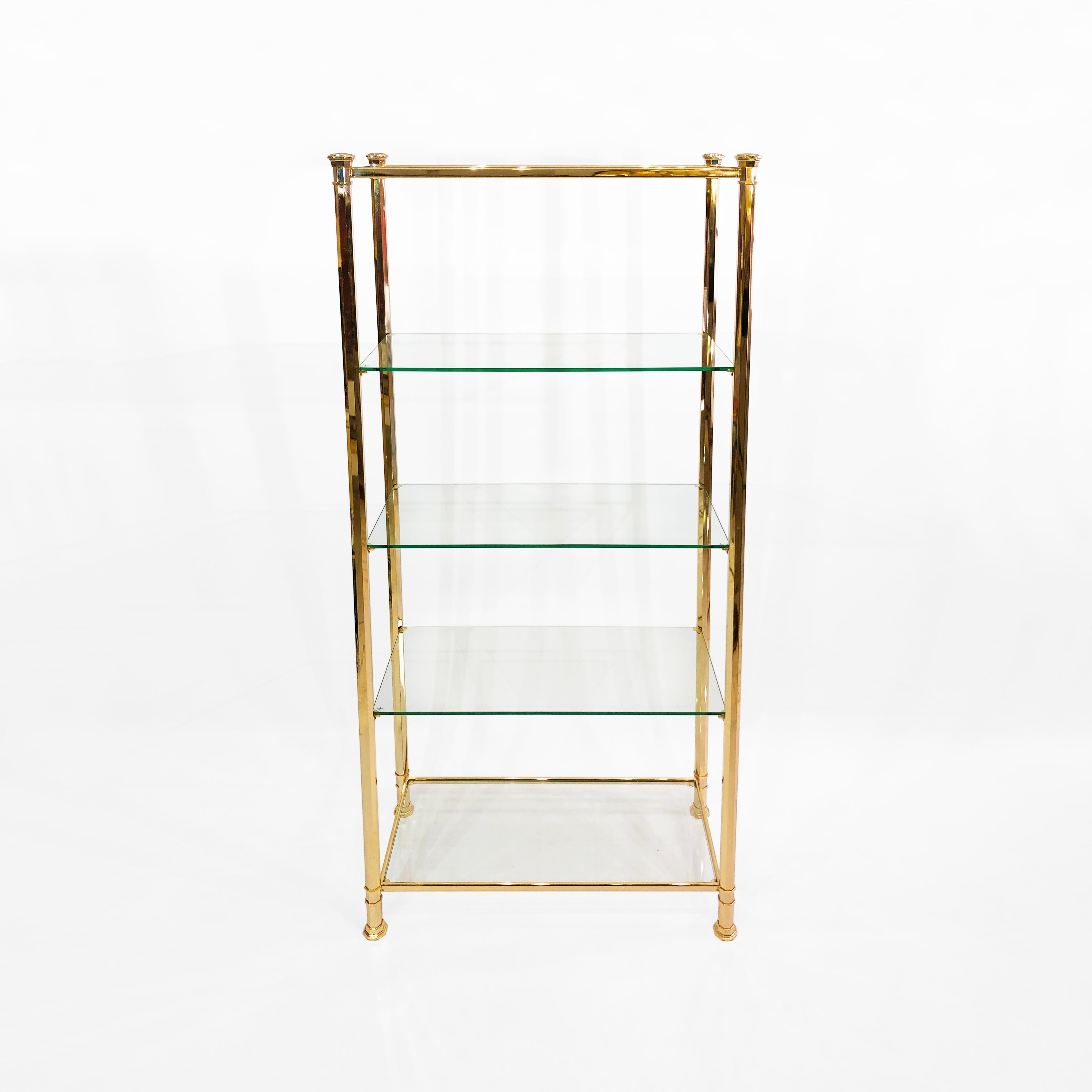 This tall étagère, manufactured in an elegant polygonal brass by Kesterport, is an excellent example of the Hollywood Regency opulence of the 1970s. A brass frame with regal corner details supports five floating glass shelves, making it ideal for