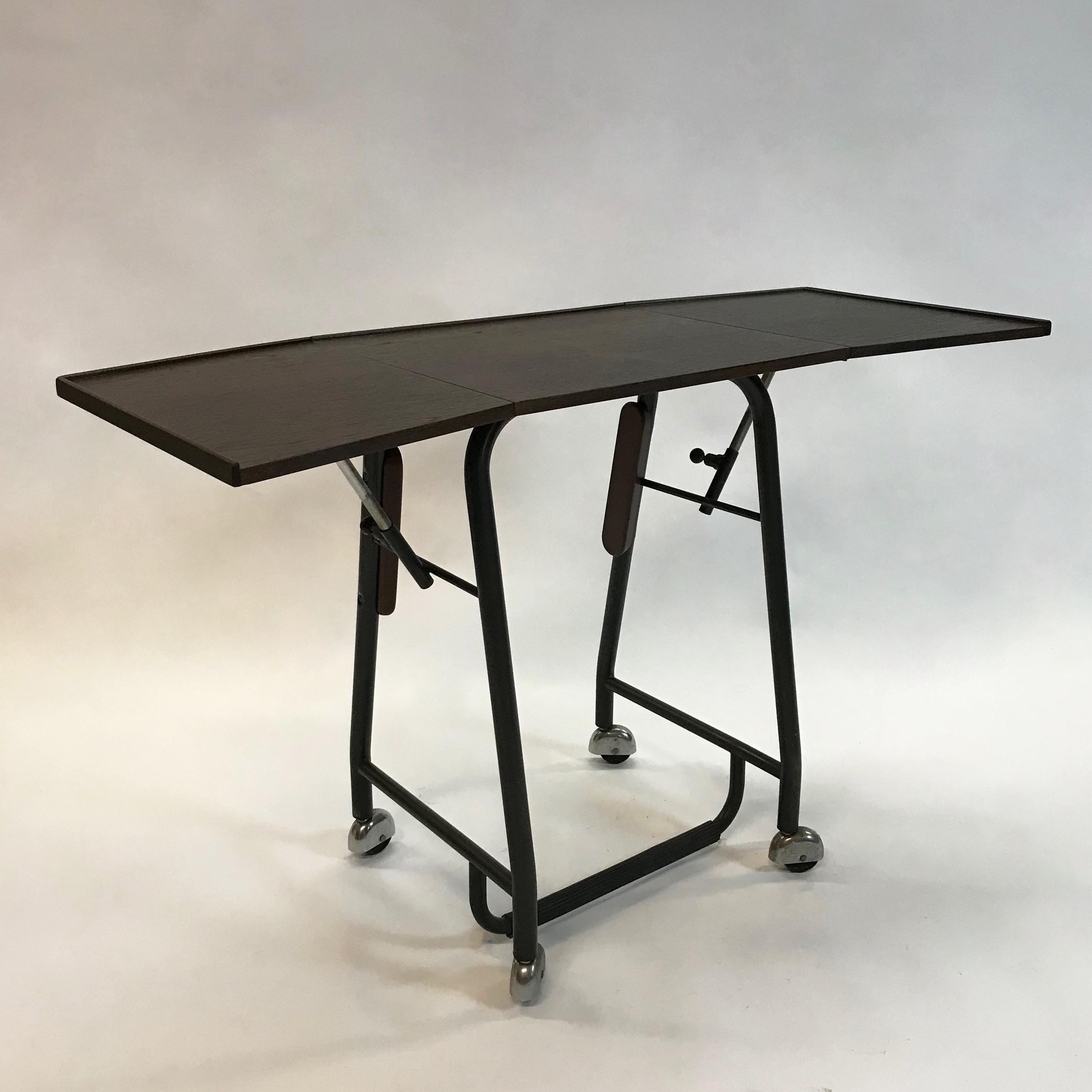 Rare, Mid-Century Modern, rolling typewriter table by Jorgen Rasmussen for Knoll features a gate-fold, teak top with a lip for paper, metal base with rubber coated footrest. When folded it measures 18.5 inches wide. One sits at the table with the