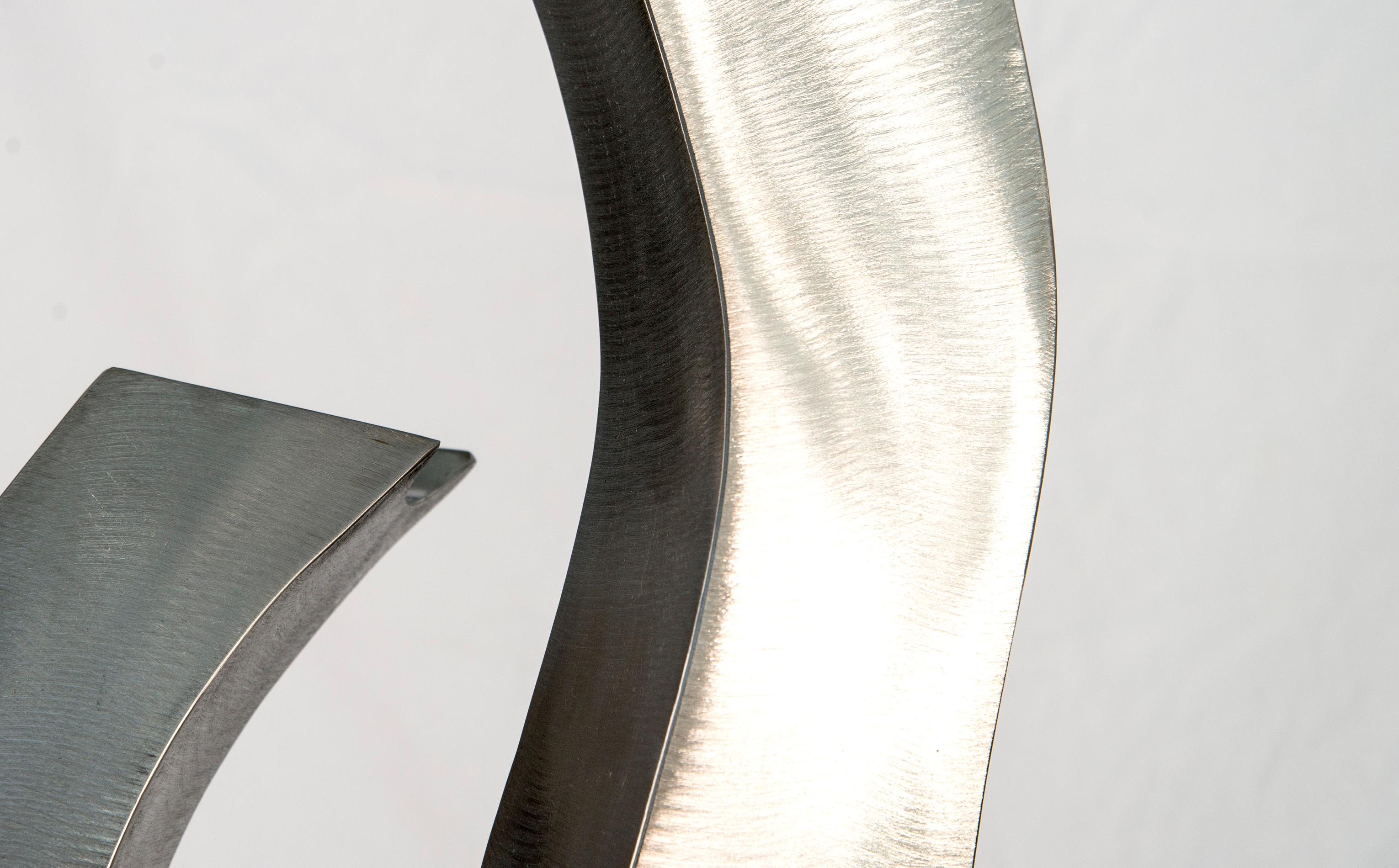 Les élégantes courbes en forme de S de cette sculpture ont été créées par l'artiste américain Kevin Robb. Trois pièces d'acier inoxydable polies et brillantes, qui se croisent, reflètent à la fois l'ombre et la lumière. Sculpteur depuis plus de 35