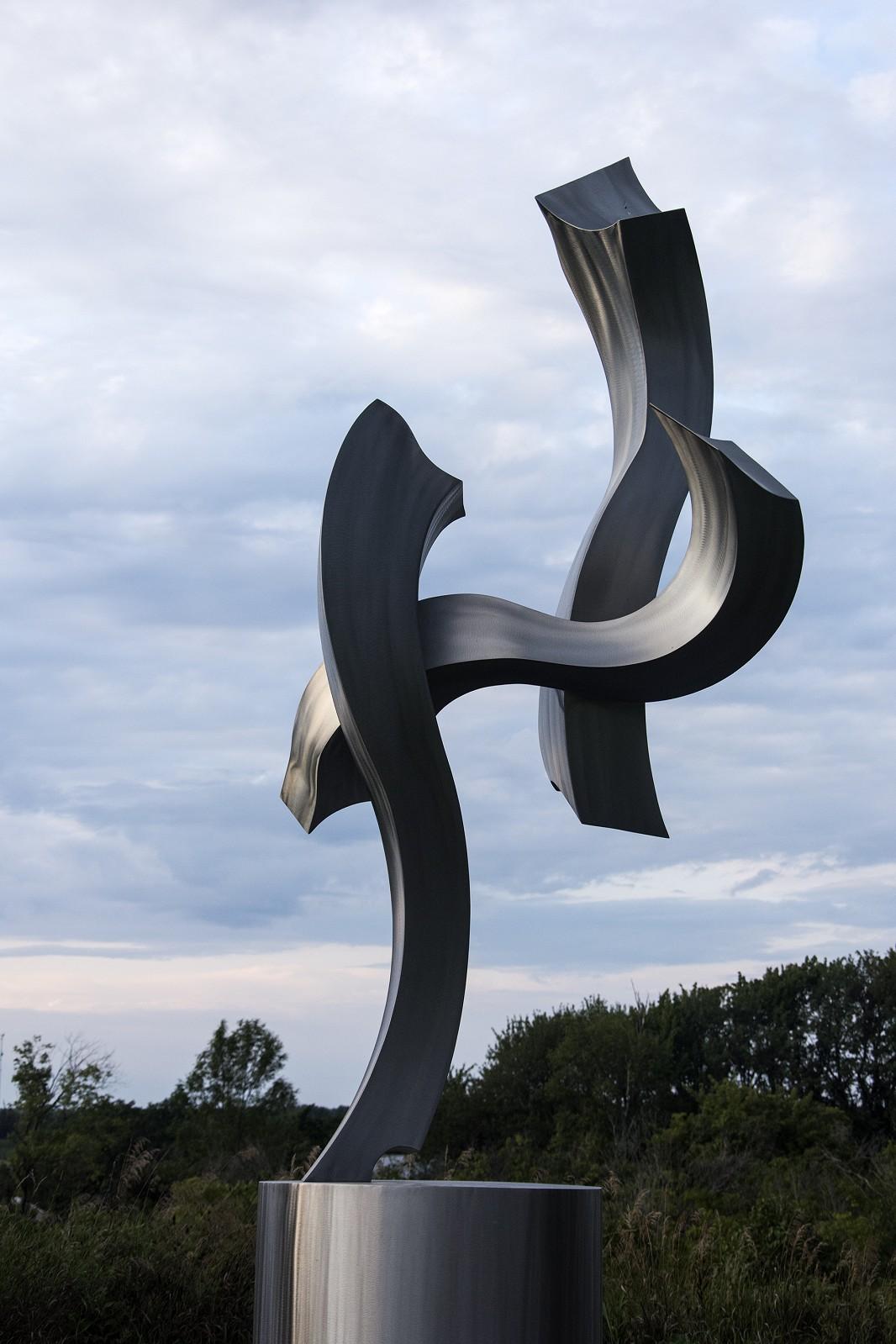 This elegant abstract metal sculpture by American artist, Kevin Robb is designed to play with natural light and shadow. Highly polished stainless steel is shaped into three dramatic curves that appear weightless. 

Robb’s work reflects a deep