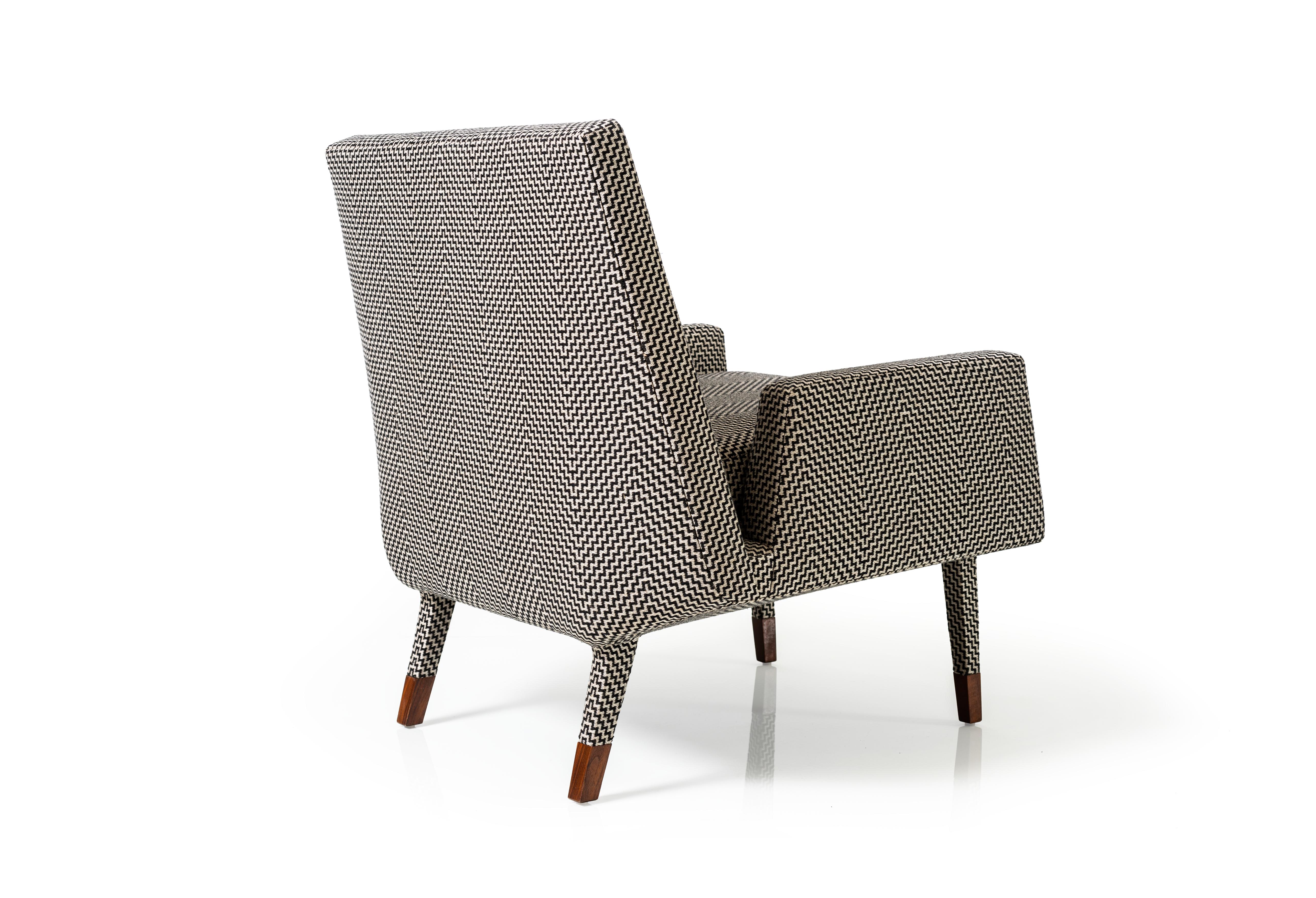 The Angott Club Chair has a softness and fluidity that is enhanced by the fully upholstered form. Fabric covers every part of the piece, including the chamfered base and a portion of the legs before they transition seamlessly to solid American Black