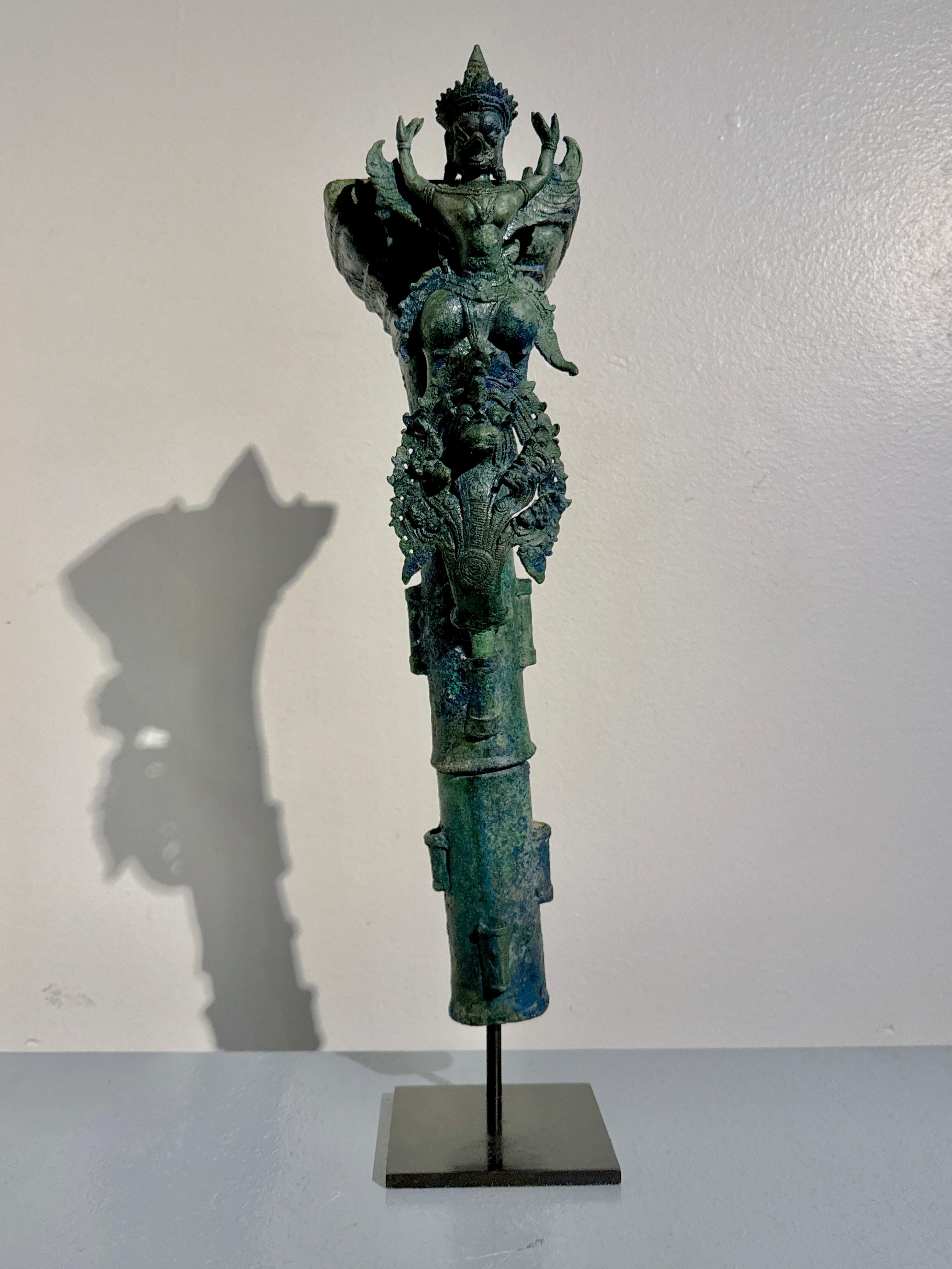 A large and impressive Khmer cast bronze finial or standard featuring a fantastic image of Garuda atop Naga, Angkor Period, Style of the Bayon, 12th to 14th century, Cambodia.

The tall standard or finial is composed of two parts: the tall support,