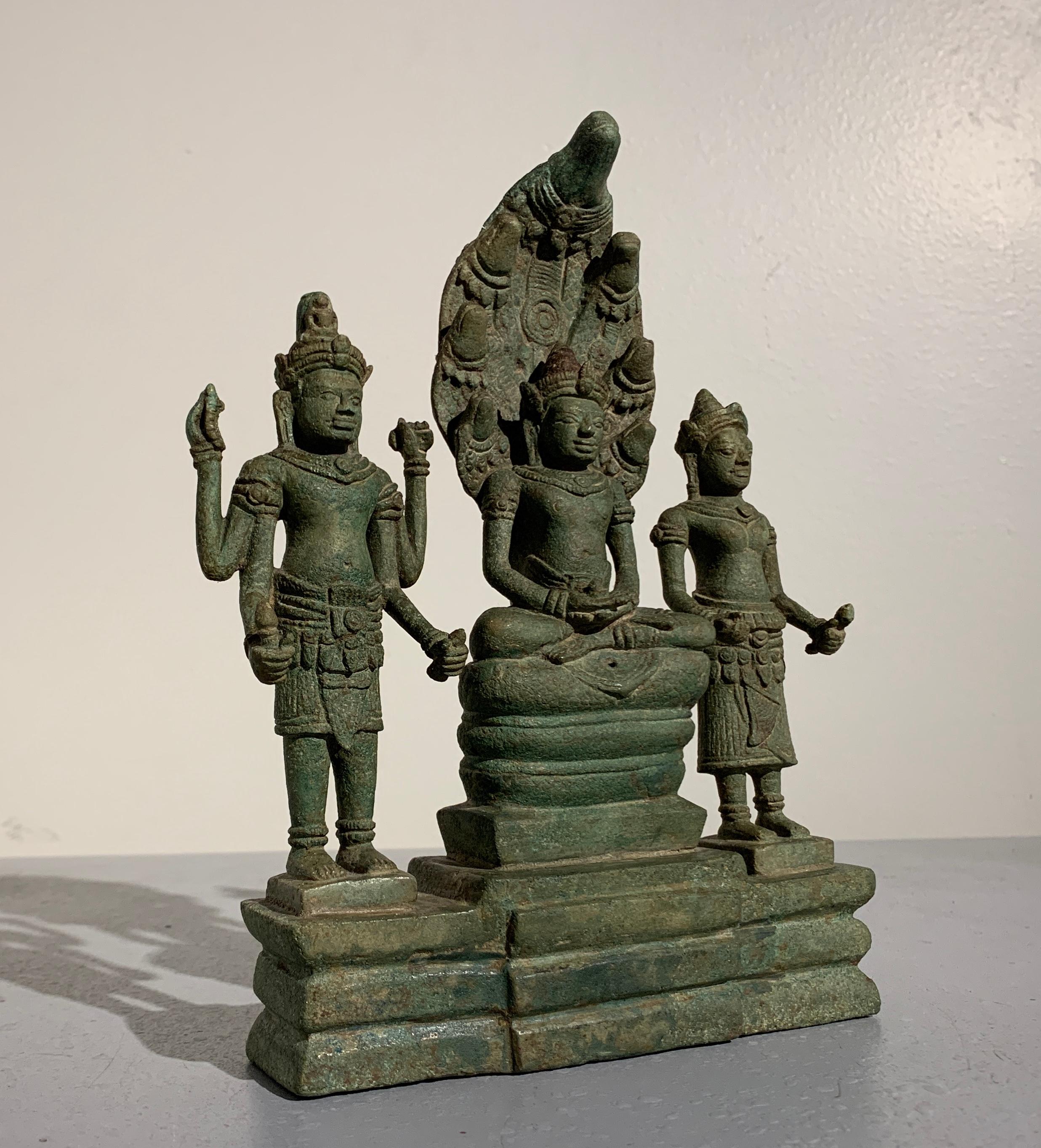 An important Khmer bronze Buddhist triad group featuring an image of the Buddha sheltered by a naga, and flanked by the bodhisattvas Avalokiteshvara and Prajnaparamita, Angkor Period, Style of the Bayon, late 12th-early 13th century, Cambodia.