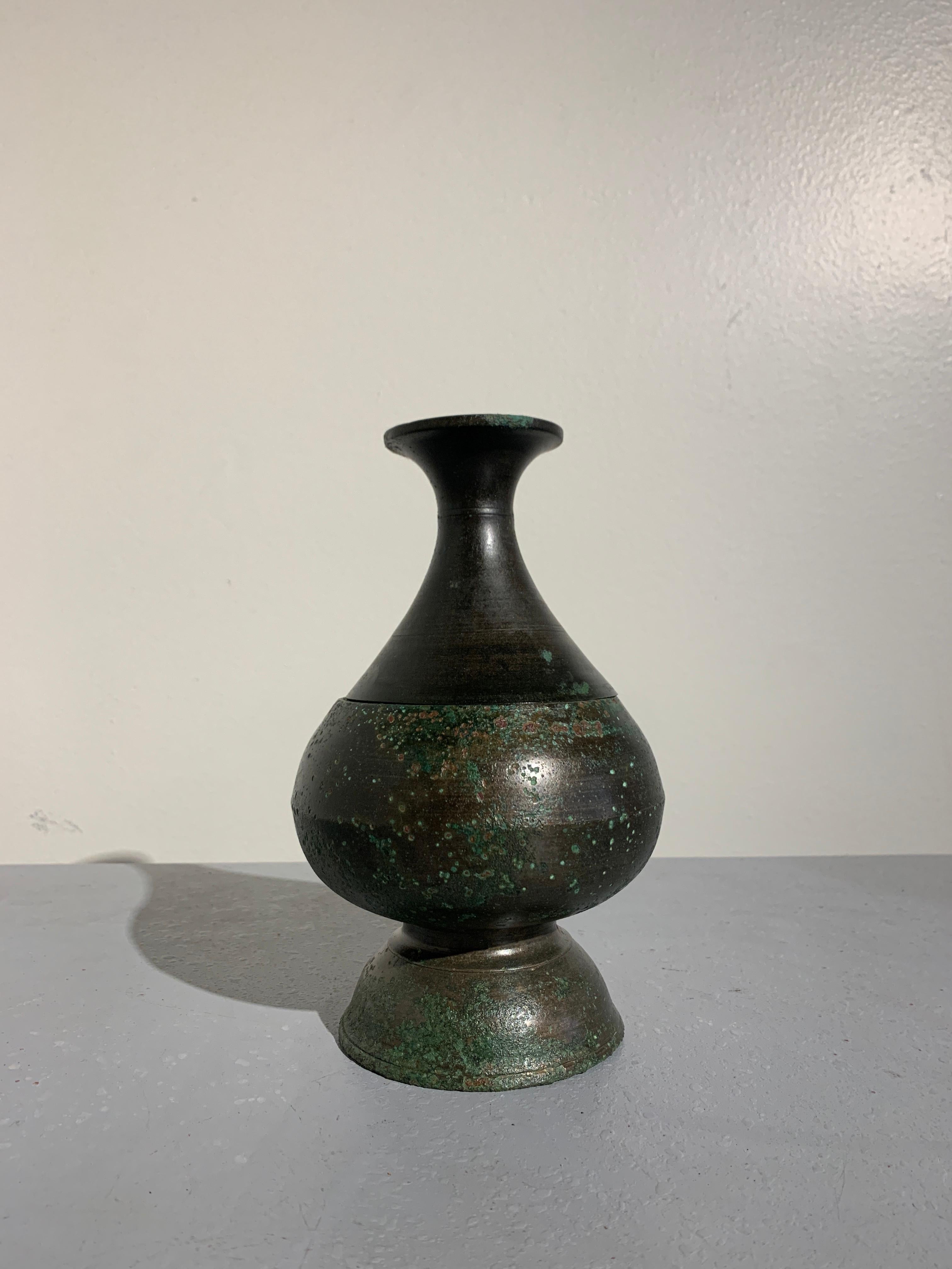 An elegant Khmer pear shaped bronze bottle vase, Angkor Period, 12th-14th century.

Crafted of bronze in two parts. When separated, the lower portion of the vase becomes an offering vessel with a pedestal foot, while the upper portion becomes a