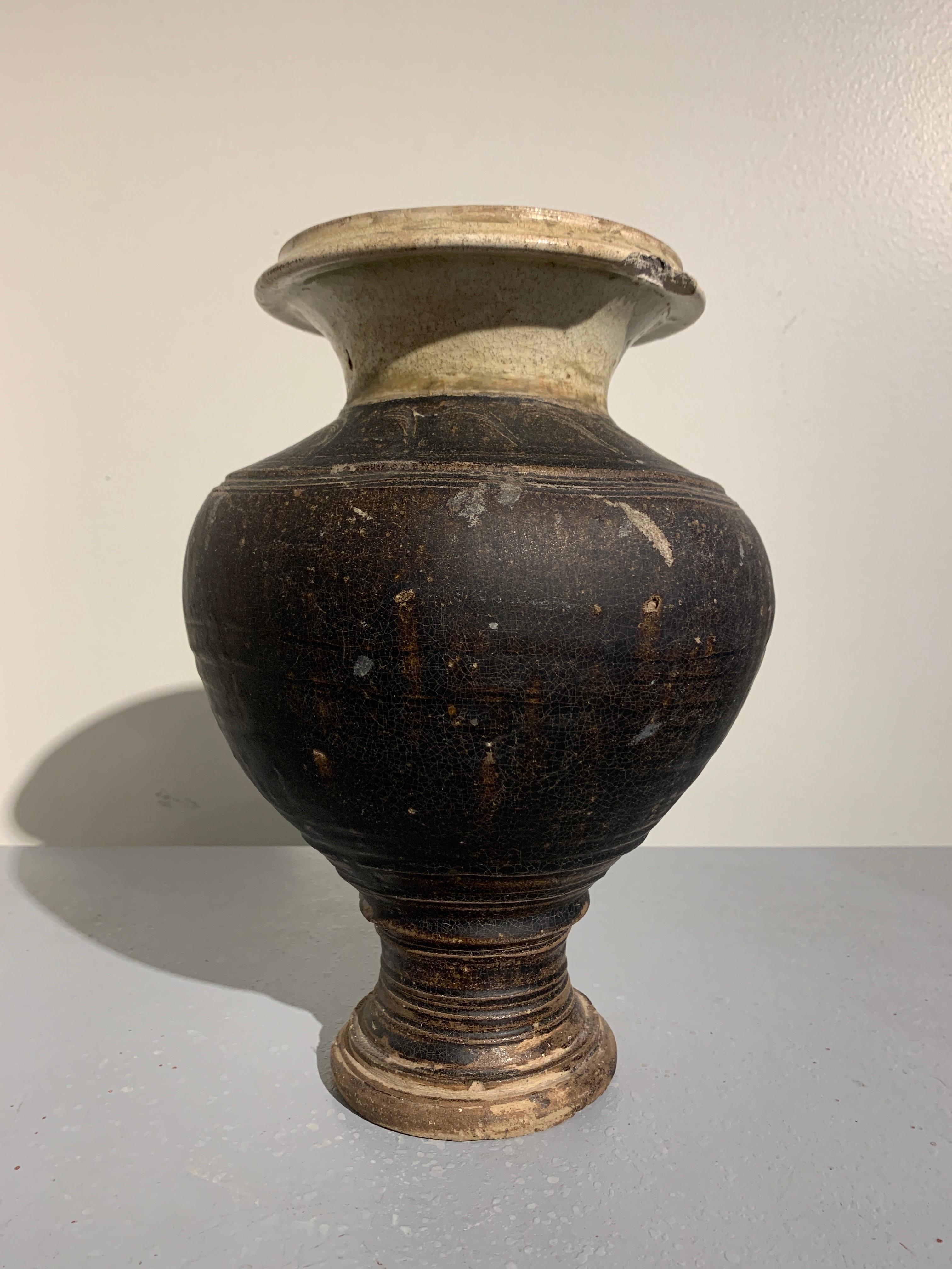 An unusual Khmer brown and celadon glazed stoneware baluster pedestal vase, Angkor Wat Period, 11th to 12th century. 

The vase of baluster form, with a wide, bulging body set on a narrow pedestal foot. The neck of the vase wide and squat, rising
