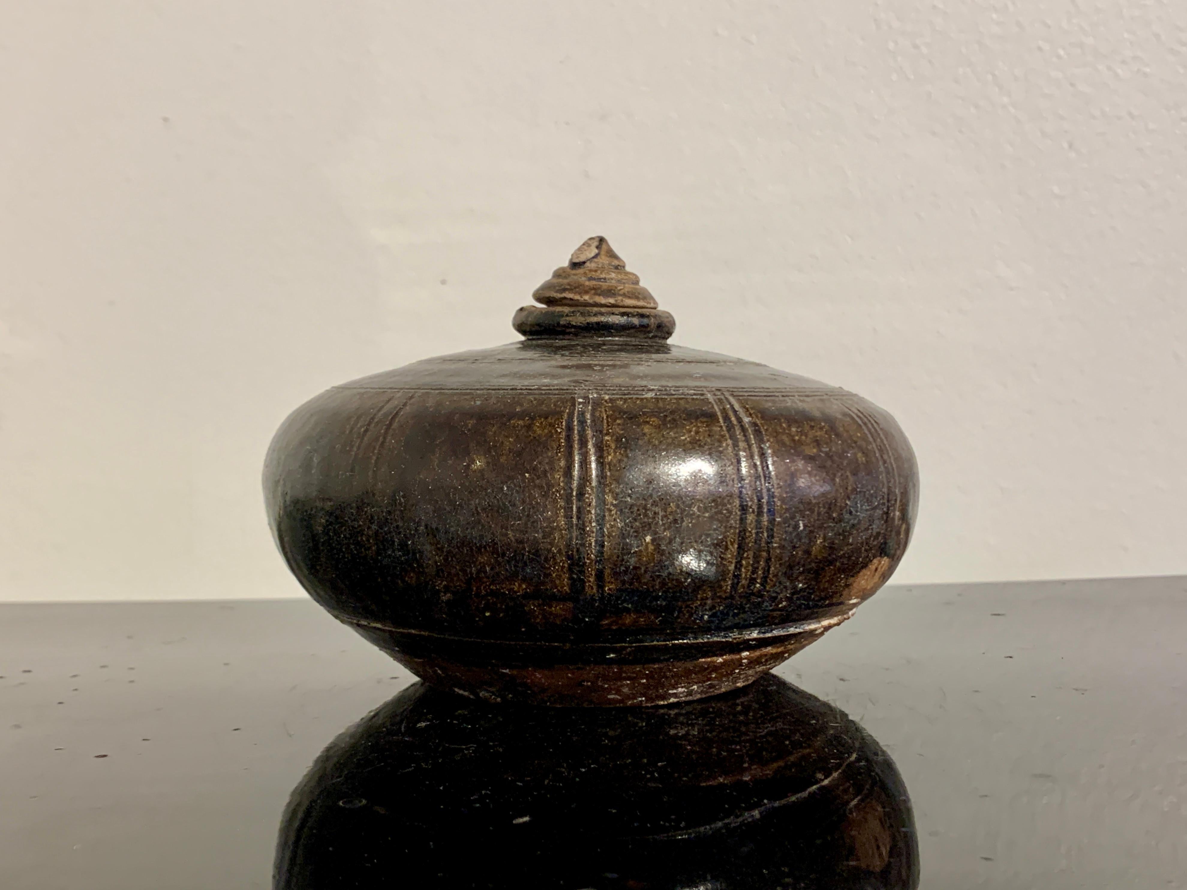 An attractive small Khmer brown glazed stoneware honey or oil pot, 12th to 14th century, Cambodia.

The small pot of compressed globular form and glazed in a deep brown glaze with yellow undertones. 
The top of the pot with three bands of incised