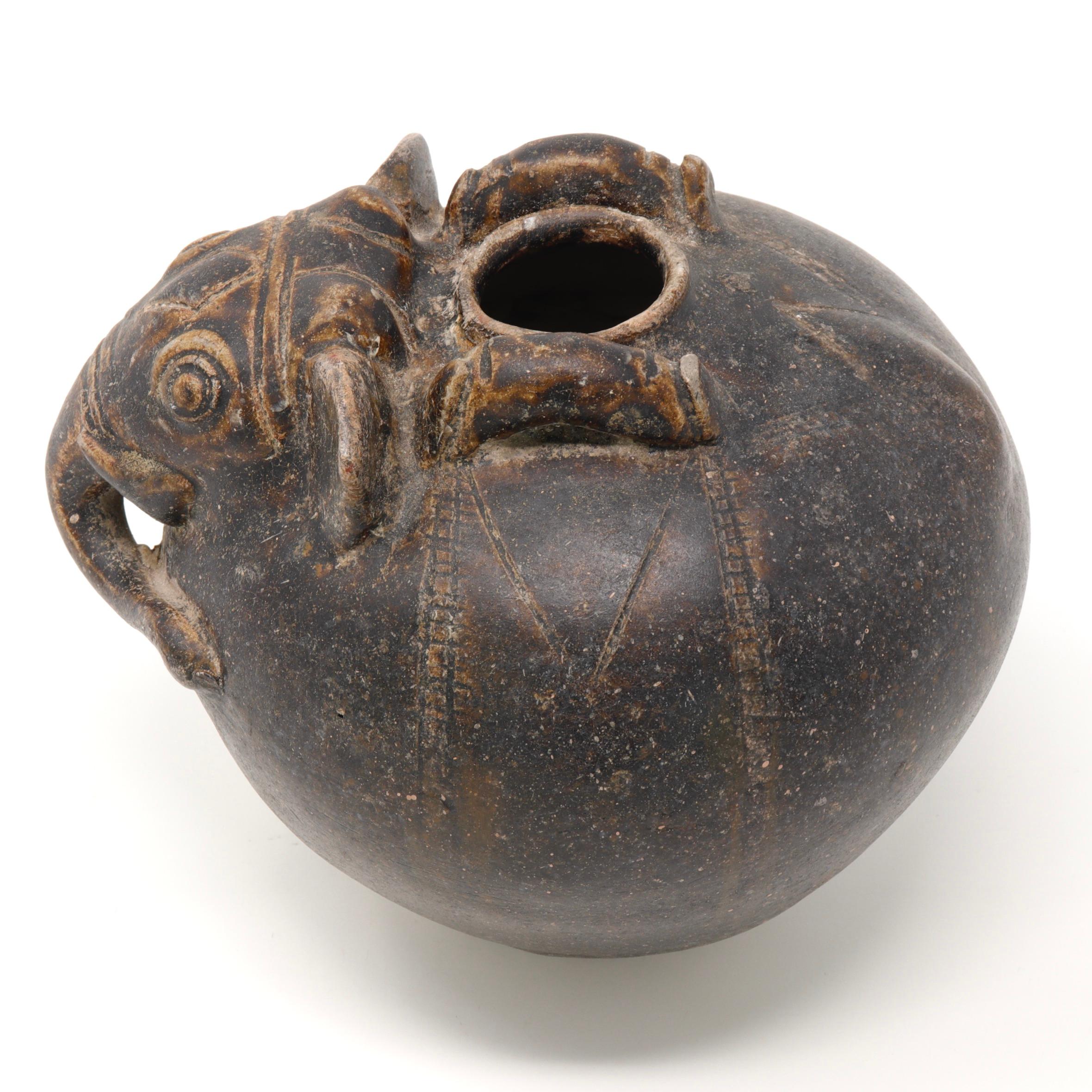 Khmer Elephant Form Lime Pot, 12th century. A globular stoneware form with narrow aperture on top for the slaked lime. The pot modeled after an elephant’s head at the shoulder with trunk, tusks and short ears and having incised markings and two