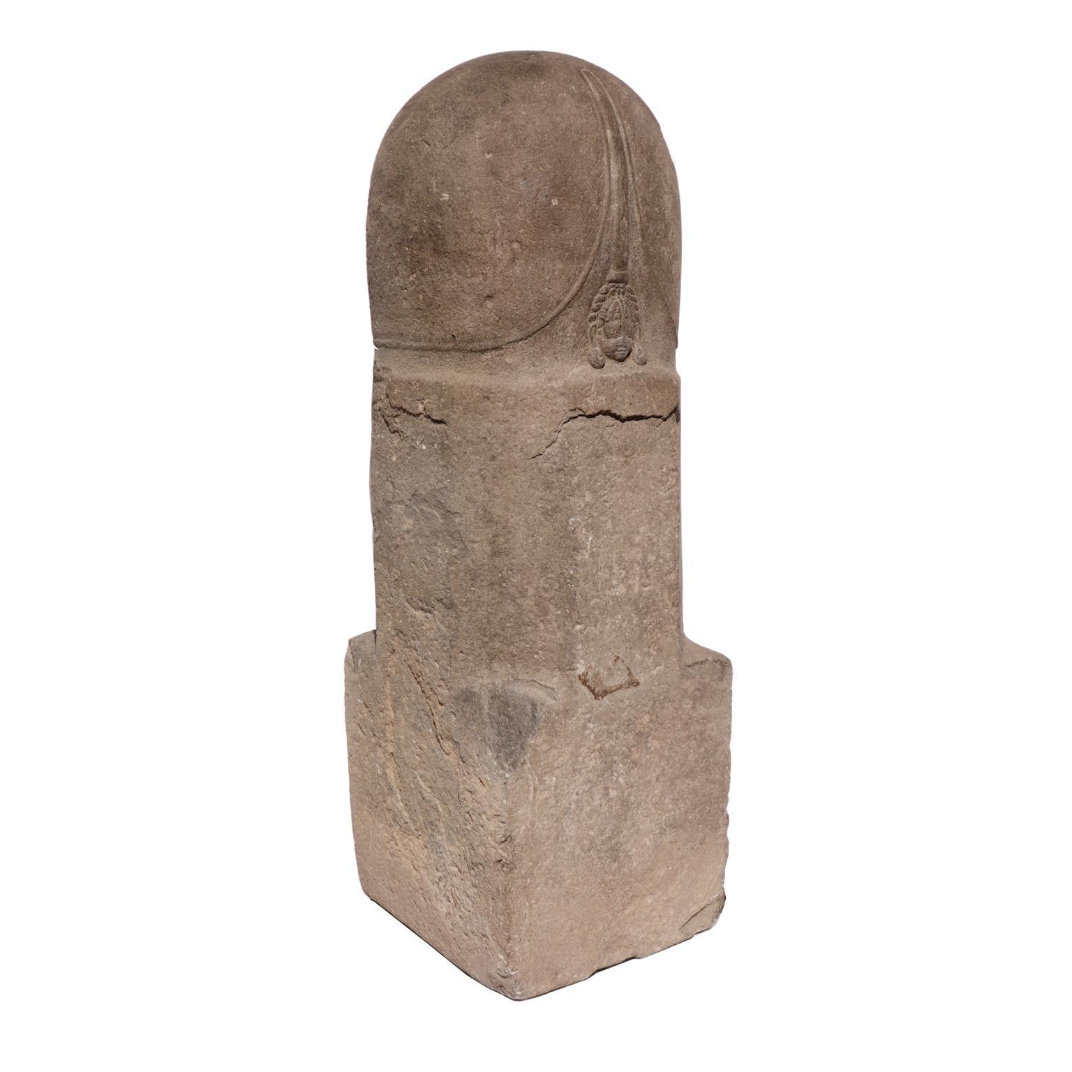 Khmer Mukhalinga, a sandstone sculpture of a Linga fronted with a small relief face of Siva, simple form with square base, octagonal mid-section and cylindrical top representing a phallus, the immaterial form of the supreme deity Siva. 
Pre-Angkor