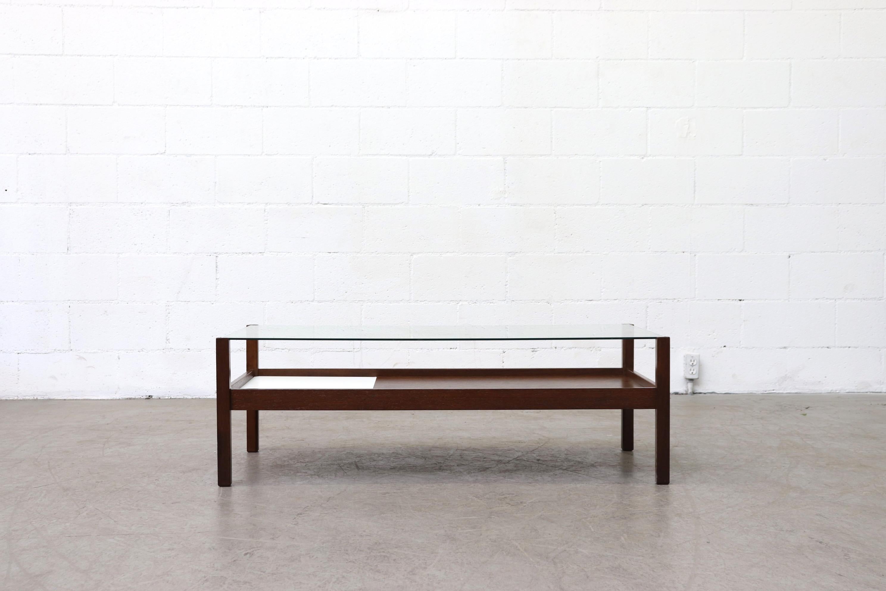 Dark teak inset glass coffee table with lower shelf and inset white formica. Originally produced with an inset rattan basket, later replaced with white formica. Lightly refinished. Frame in otherwise original condition with some wear consistent with