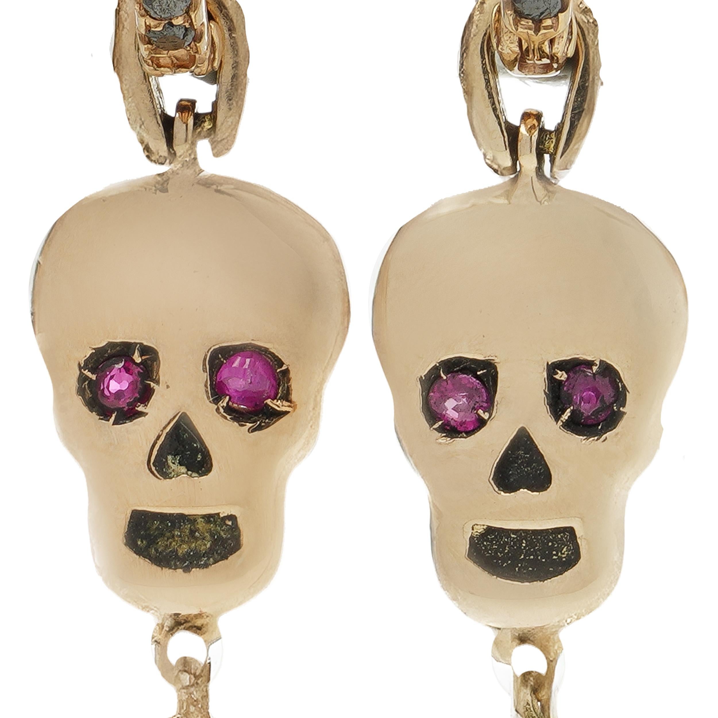 A striking pair of contemporary earrings by KIAIA, finely crafted in 18 karat yellow gold. Each earring features a stylised skull motif set with round-cut ruby eyes, exhibiting a vivid pinkish-red hue, estimated at 0.03 carats each. The skulls are