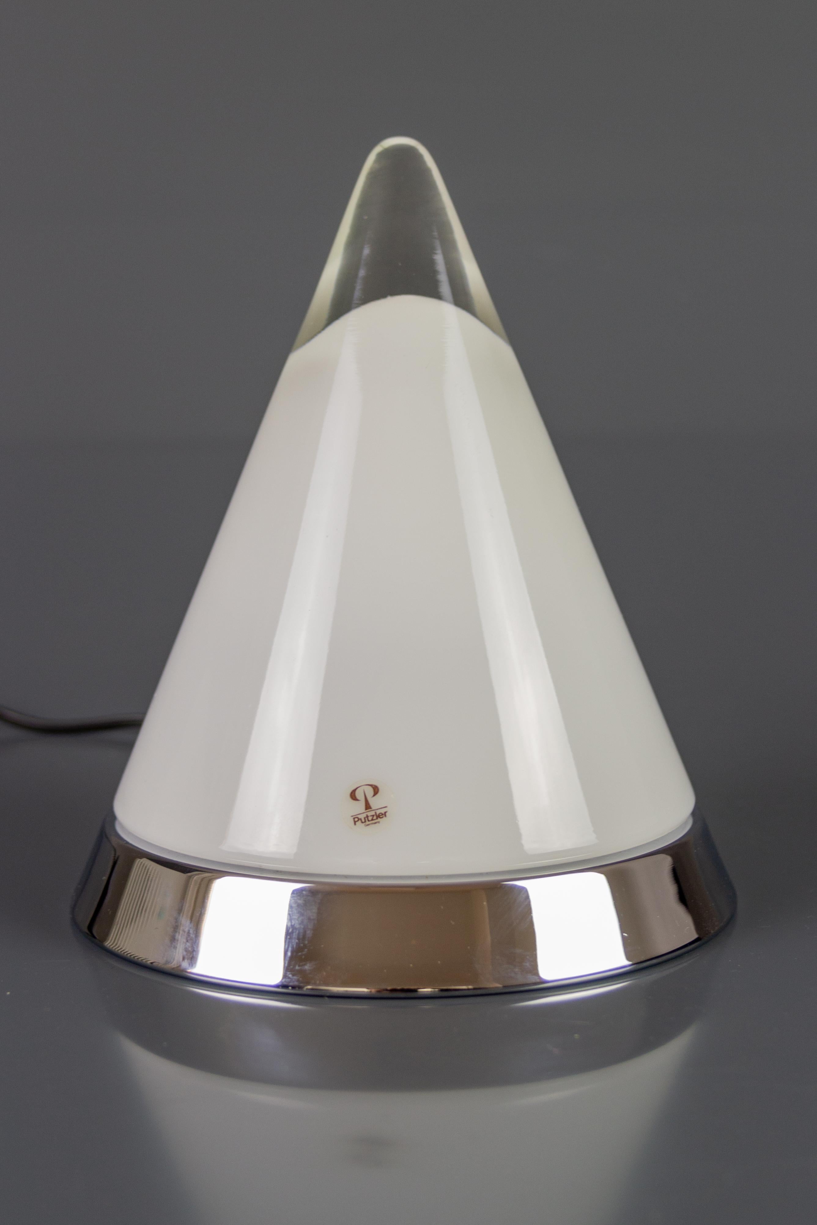 A Peill & Pulzer Kibo model table lamp. The pyramid-shaped lamp features a hand-blown clear and white shining opaline conical glass lampshade ascending to a transparent crystal tip. Round chrome base with a white painted metal holder. 
Dimensions: