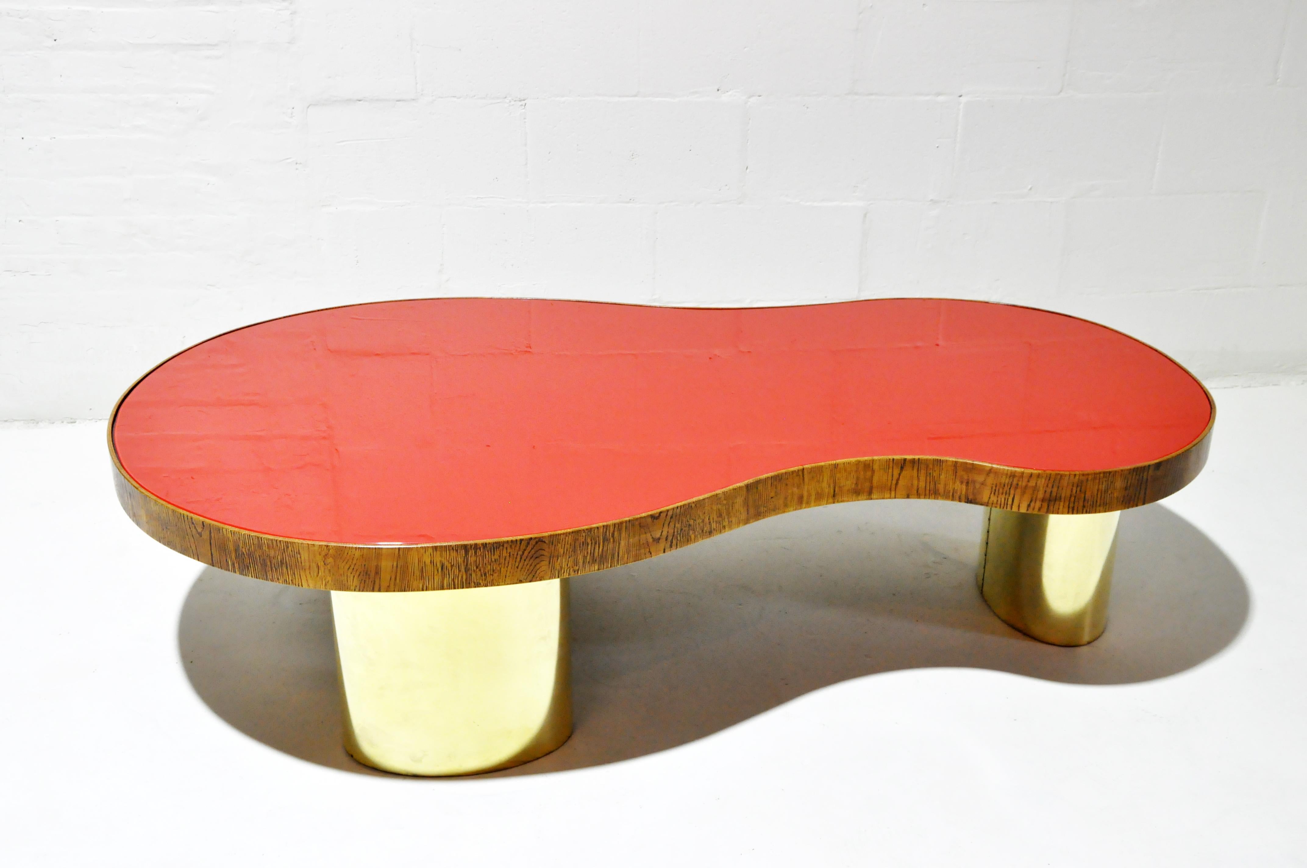 A rare kidney-shaped coffee table with a red glass top, cylindrical brass legs and walnut edge trim.
       