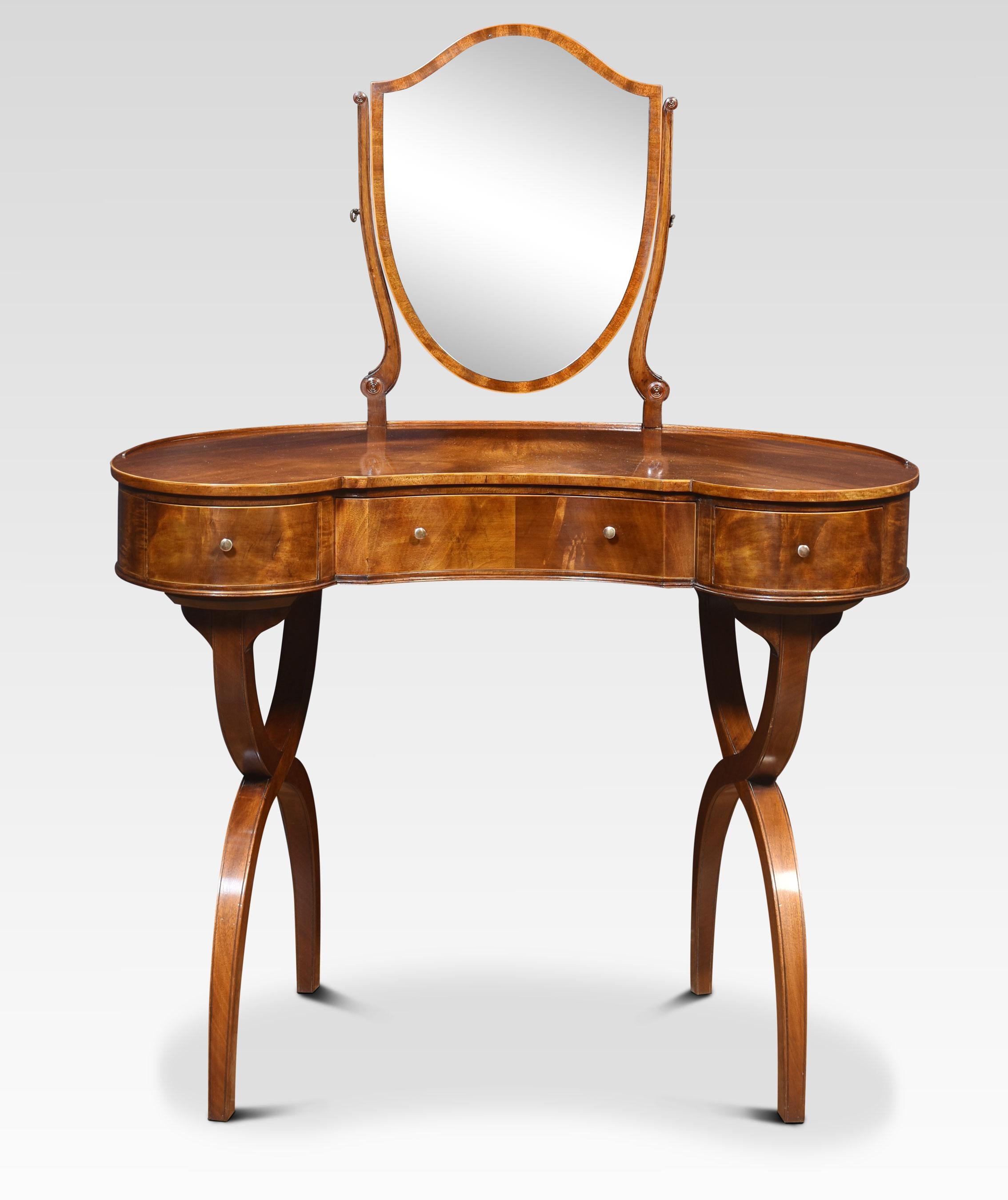 Mahogany kidney-shaped lady’s dressing table, the shield-shaped adjustable mirror supported on slender mahogany supports. To the well-figured kidney-shaped top. To the frieze fitted with three drawers with brass handles. All raised up on x-shaped