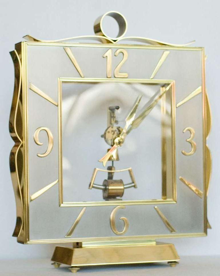 A stunning midcentury Regency styled mantel clock with a brass case and floating glass paneled center stage with an electromagnetic movement, with a brushed steel square chapter ring with a Roman numeral chapter ring and pierced decoration