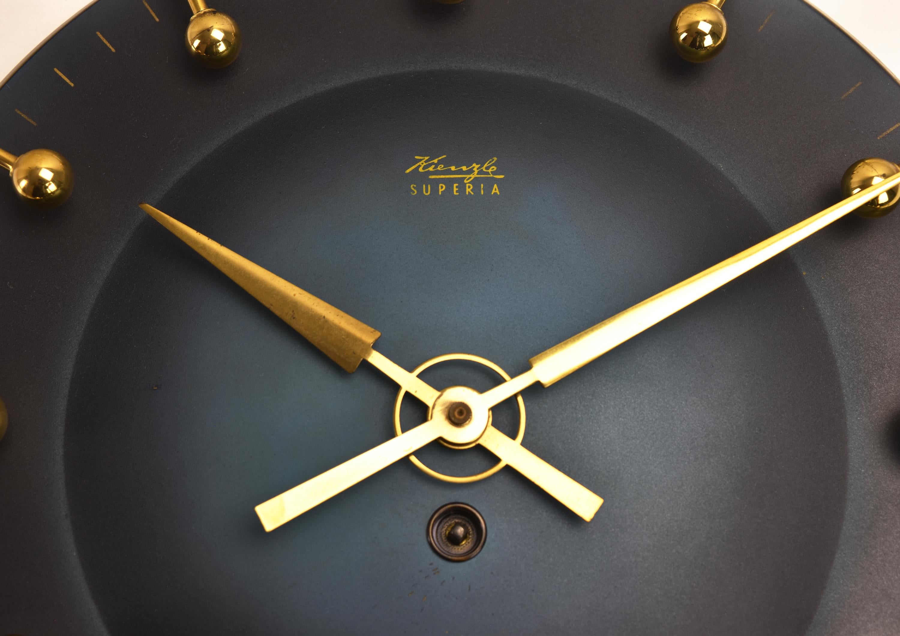 This ultra-rare Kienzle Superia wall clock from the 1950s exemplifies the modernist aesthetic with an atomic, sunburst design. Its striking black and brass accents enhance the Hollywood Regency style, making it a true statement piece for any