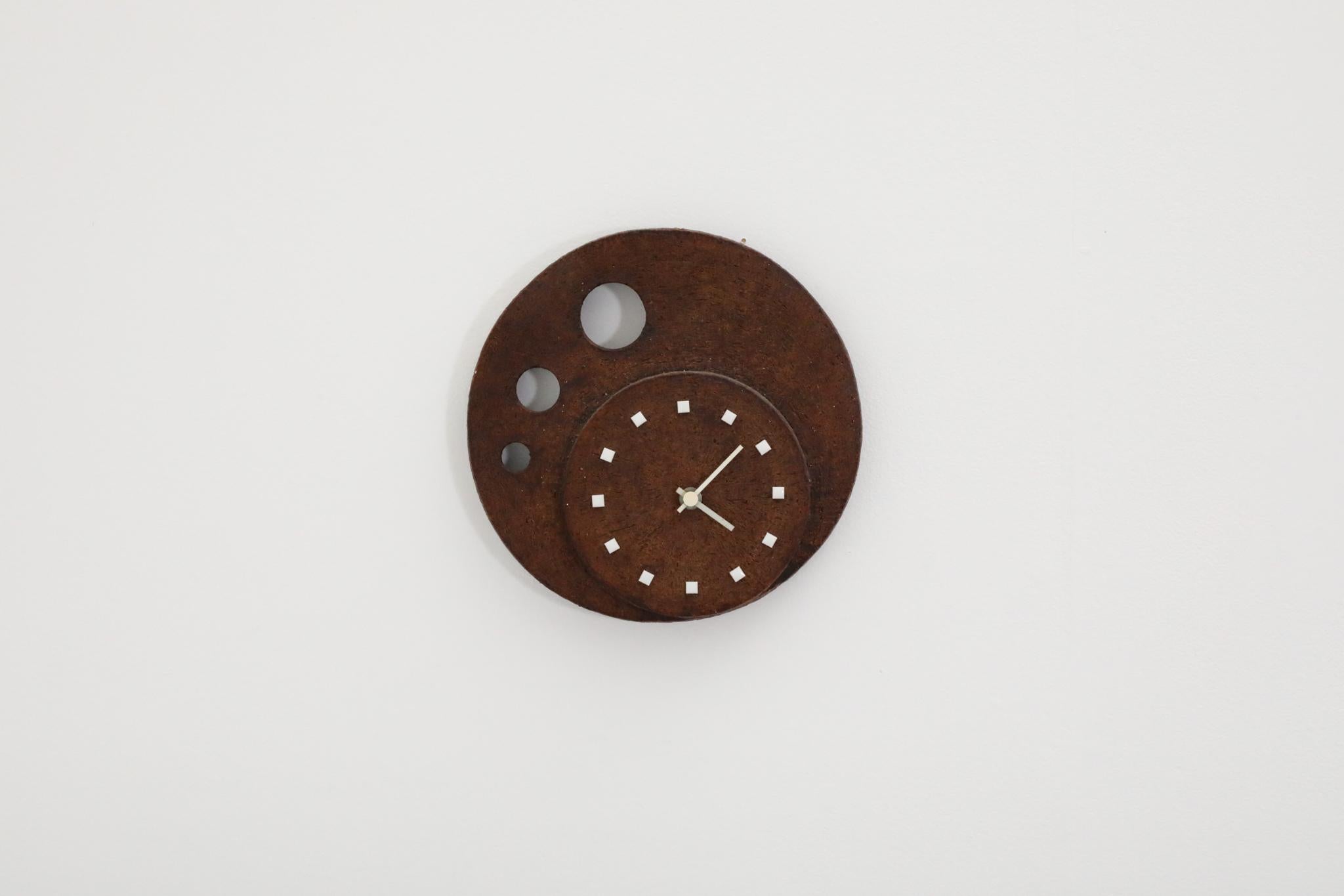 A striking German Mid-Century wall-mounted clock from the 1970s, masterfully crafted by Kienzle Uhren. This clock stands out for its bold, sculptural form, featuring a textured matte brown ceramic glaze and geometric circle cut-outs.

Designed in a