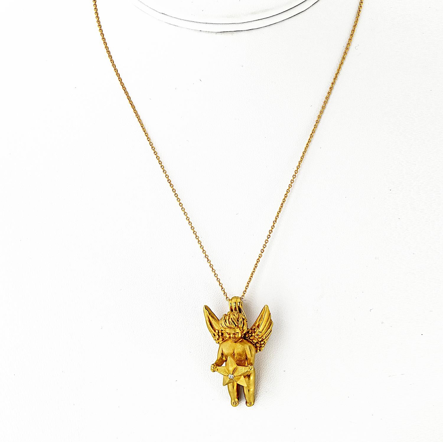 Este colgante de oro amarillo macizo de 18 quilates, una hermosa pieza simbólica y coleccionable de Kieselstein-Cord, presenta un ángel esculpido con gracia que sostiene una estrella. En el centro de la estrella hay un único diamante redondo, que