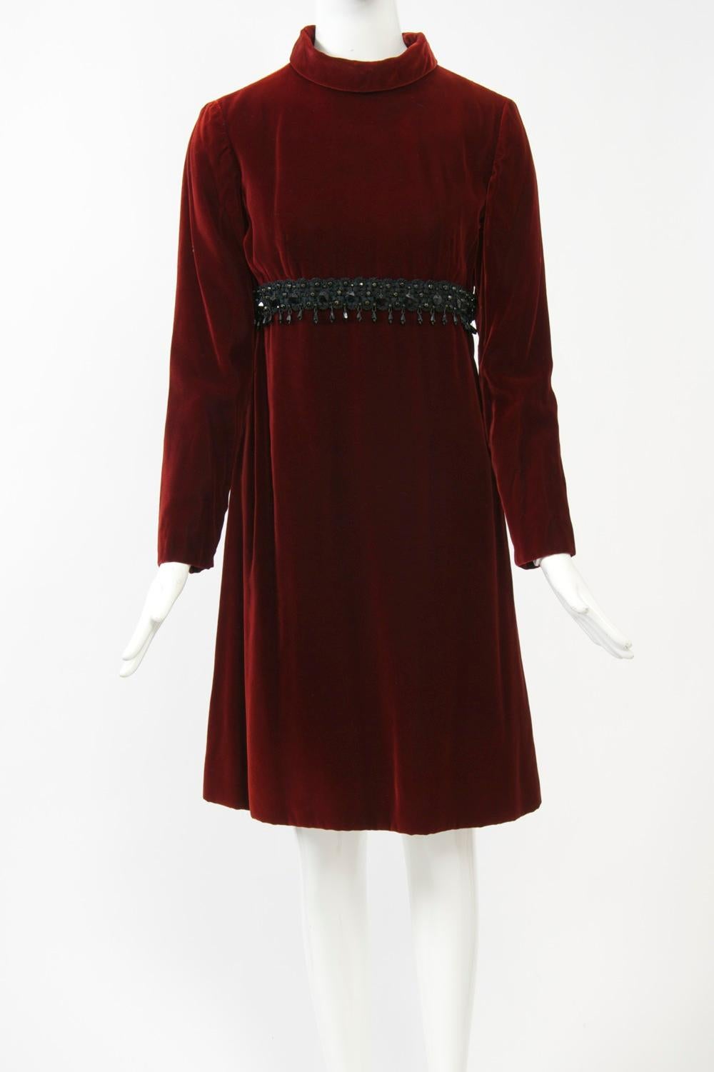 Rich burgundy velvet 1960s dress by Kiki Hart featuring an empire bustline trimmed with a band of black soutache and jet beads. A rolled turtleneck, narrow, set-in sleeves, and an A-line skirt complete the look. Fully lined. Back zipper. Approximate