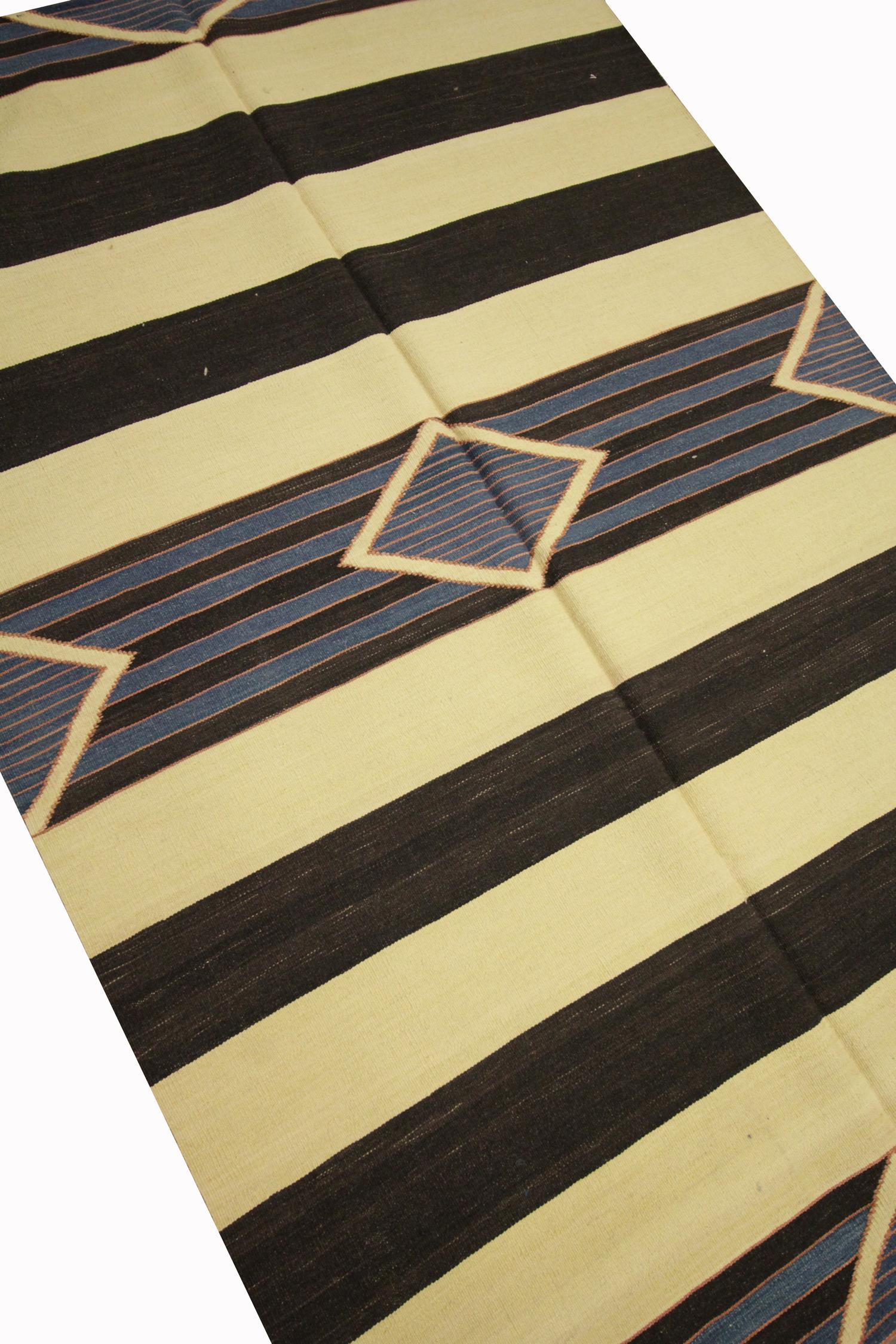 This Modern Rug is a fine wool Kilim woven by hand in India in the early 21st century. The design has been woven with a simple colour palette of cream, black and blue and features a stripe pattern with diamonds and triangles dotted and the centre