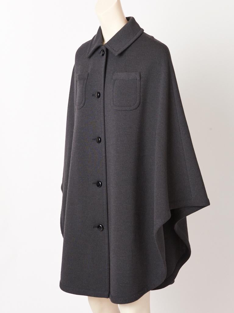 Kimberly Knit, charcoal grey, double knit, wool, cape, having a pointed collar, and black button closures going down the center front, with two small breast pockets detail and a ribbed wool knit edging.
